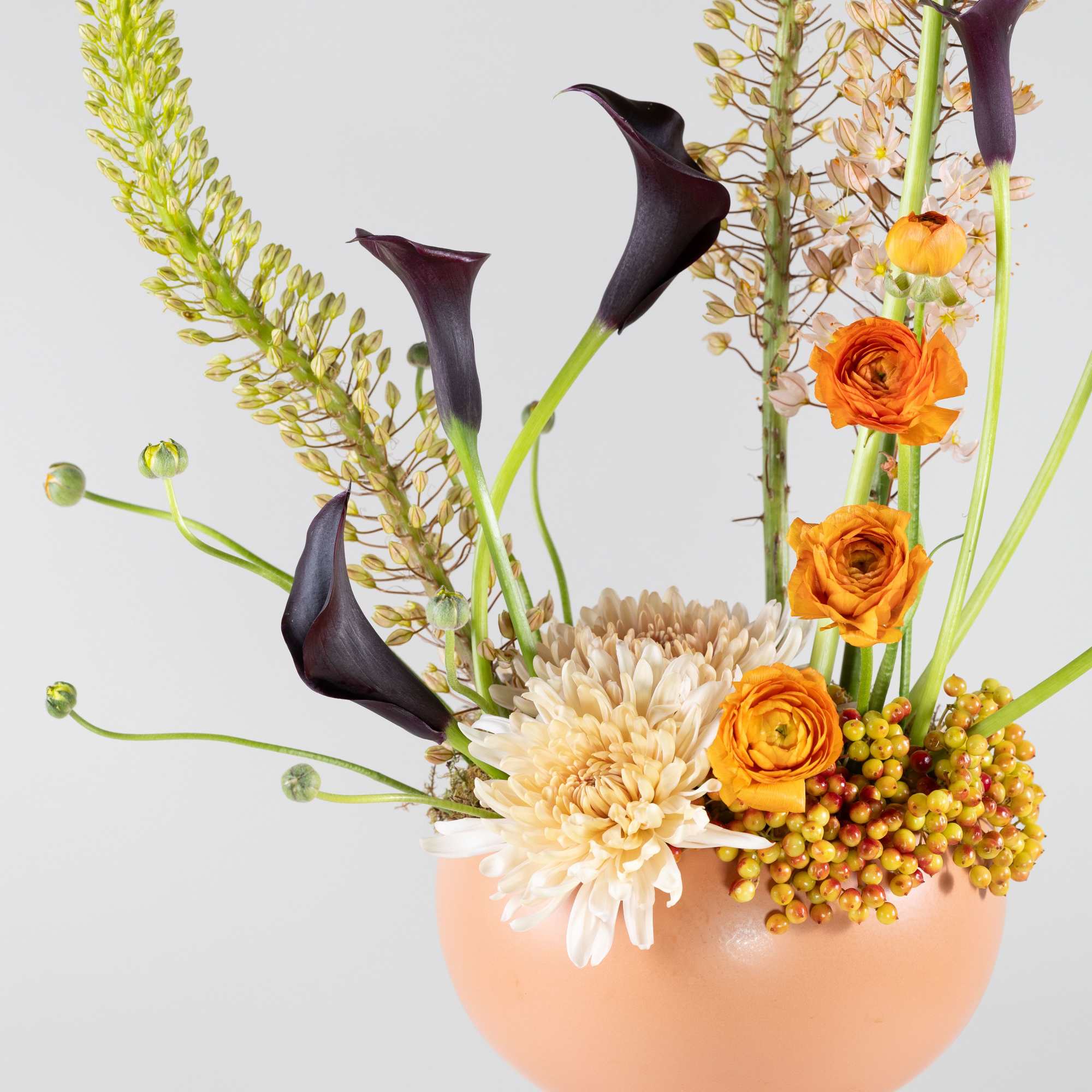 Orange and cream flowers in a peach vase with dark calla lilies