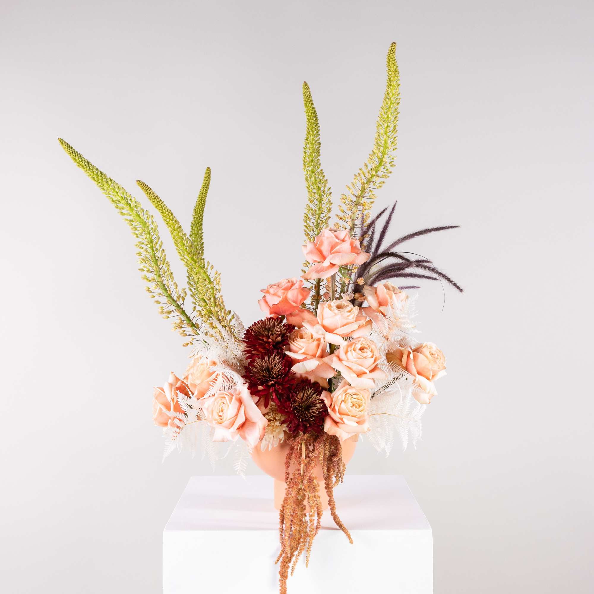 Peach roses in a vase with tall green spikes and burgundy accents