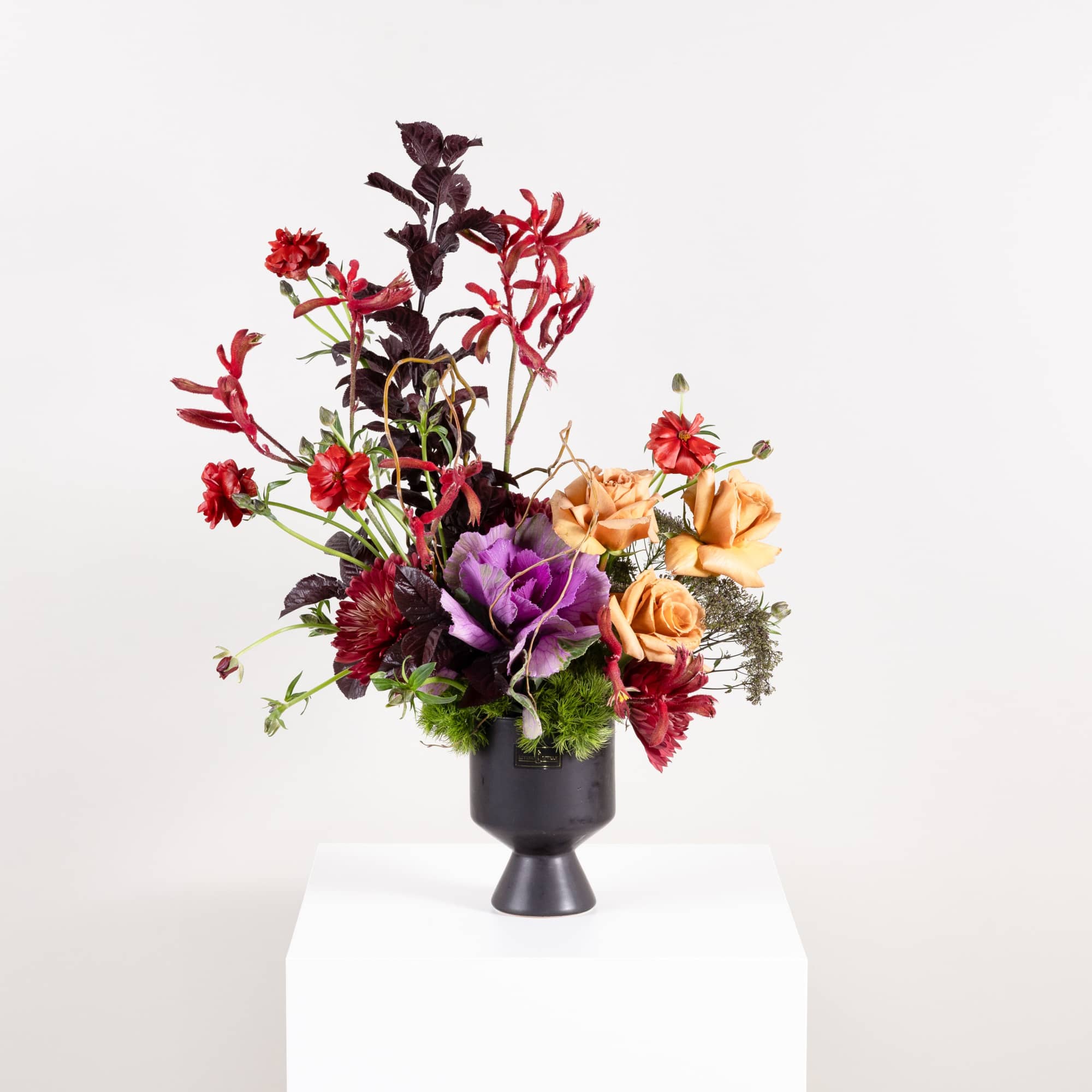 Tall floral arrangement in a black pedestal vase with red, purple, and peach blooms