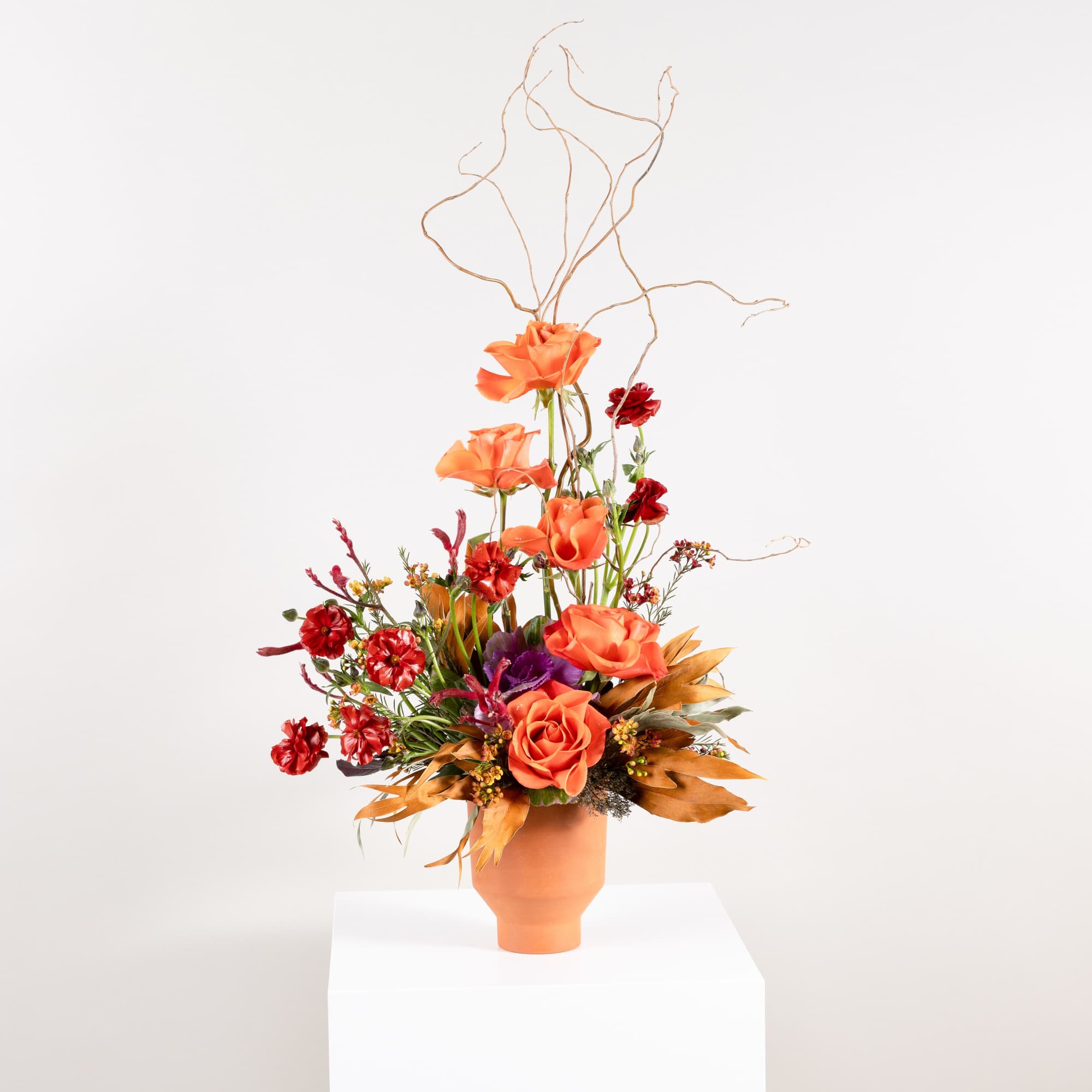 Tall orange and red floral arrangement in a terracotta vase