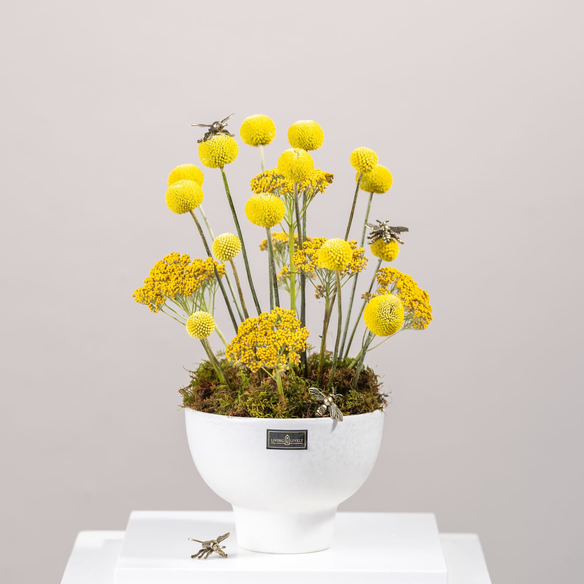 Yellow pom-pom flowers in a white pedestal vase with bee decorations