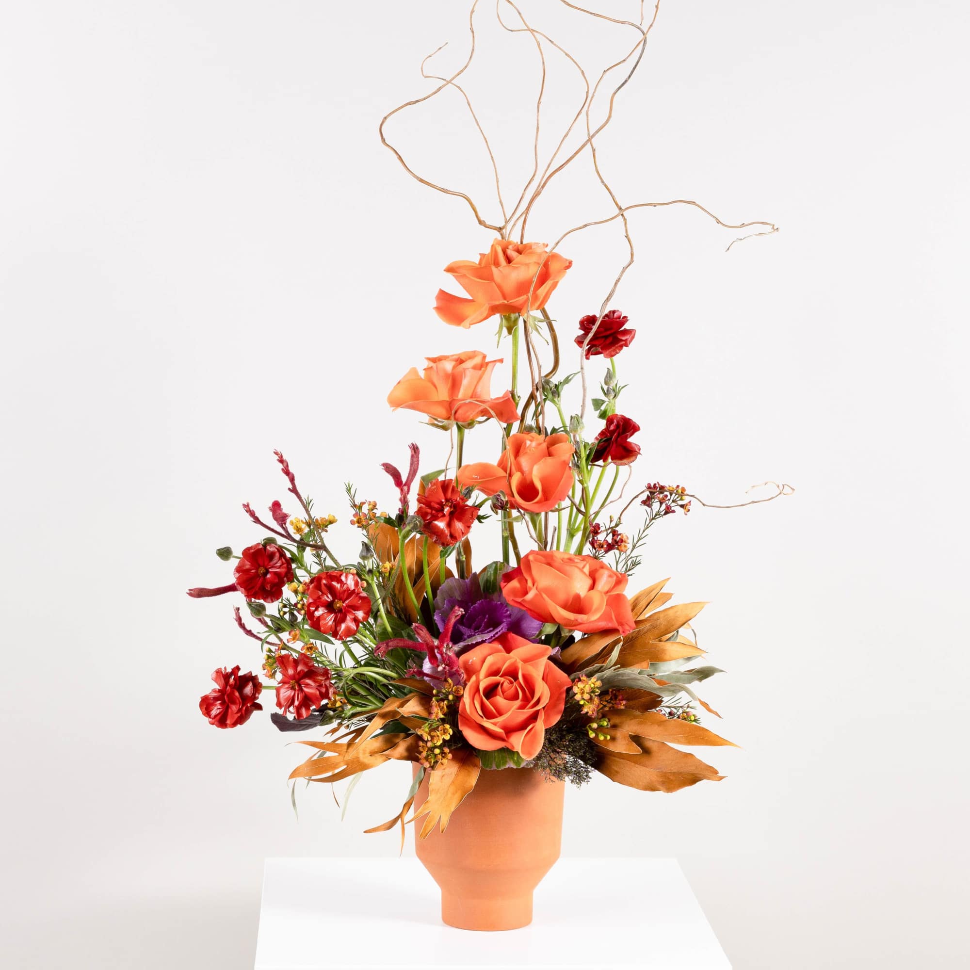 Orange and red floral arrangement in a terracotta vase with tall branches
