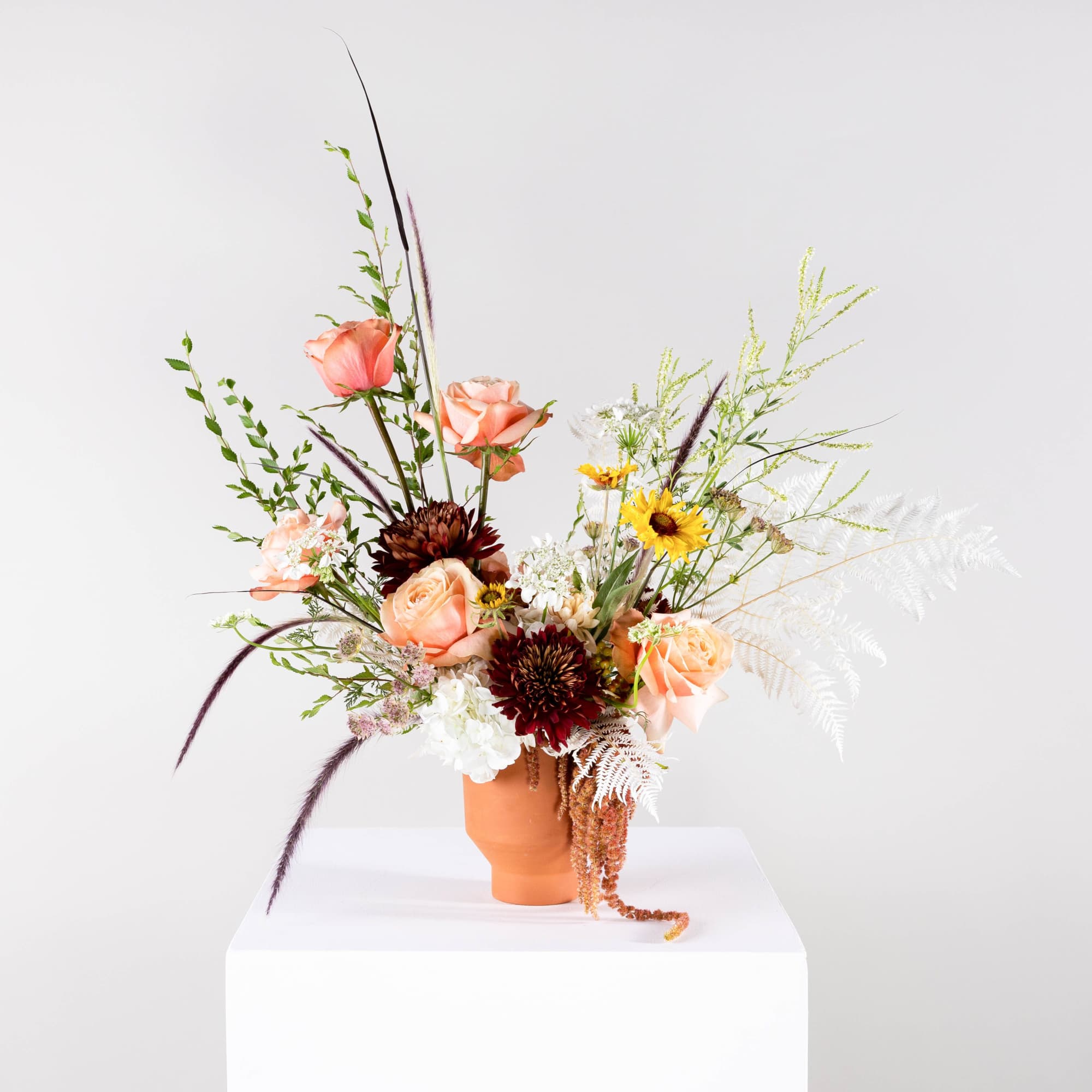 Mixed bouquet with peach roses and dark blooms in a terracotta vase