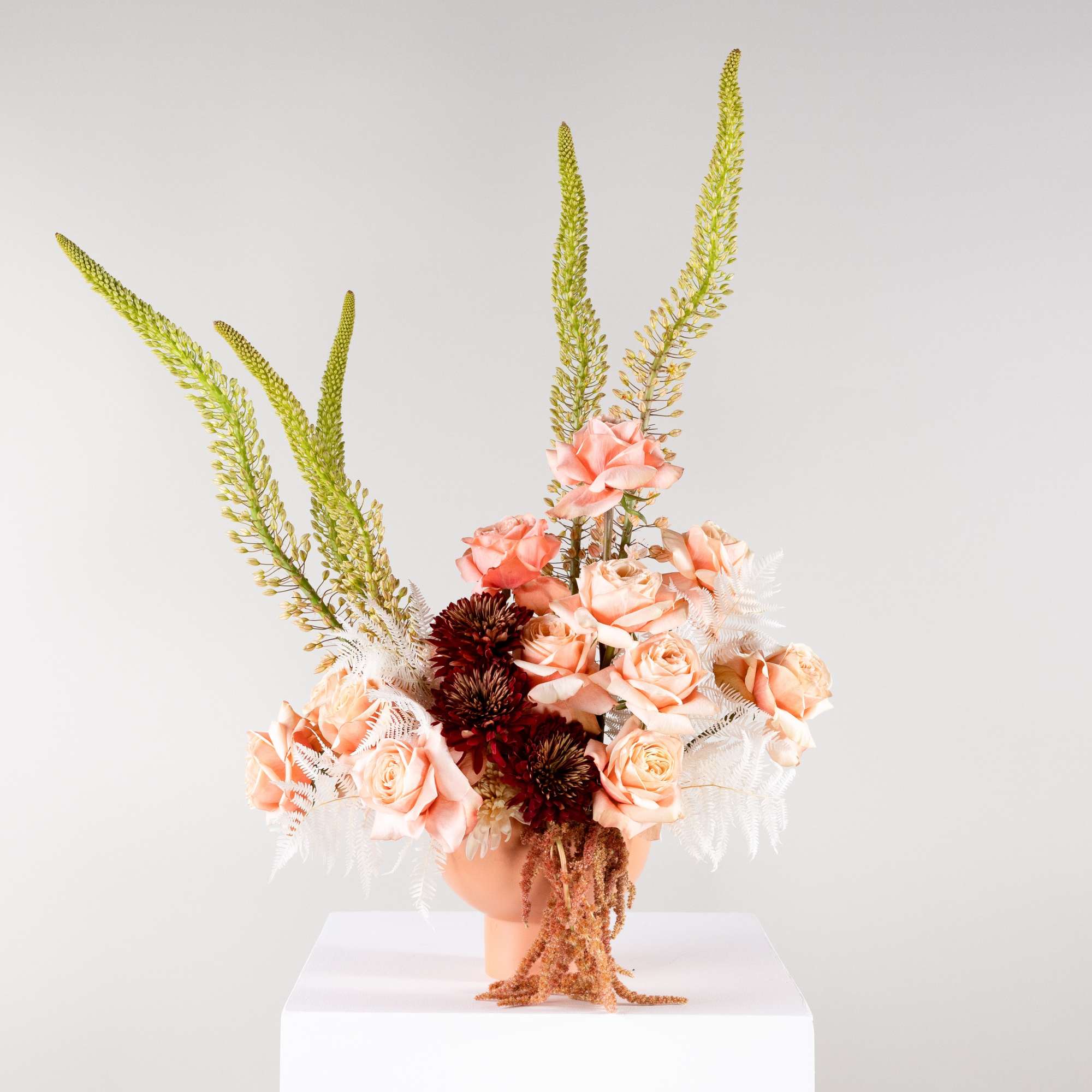 Peach roses and burgundy blooms in a vase with tall green spikes