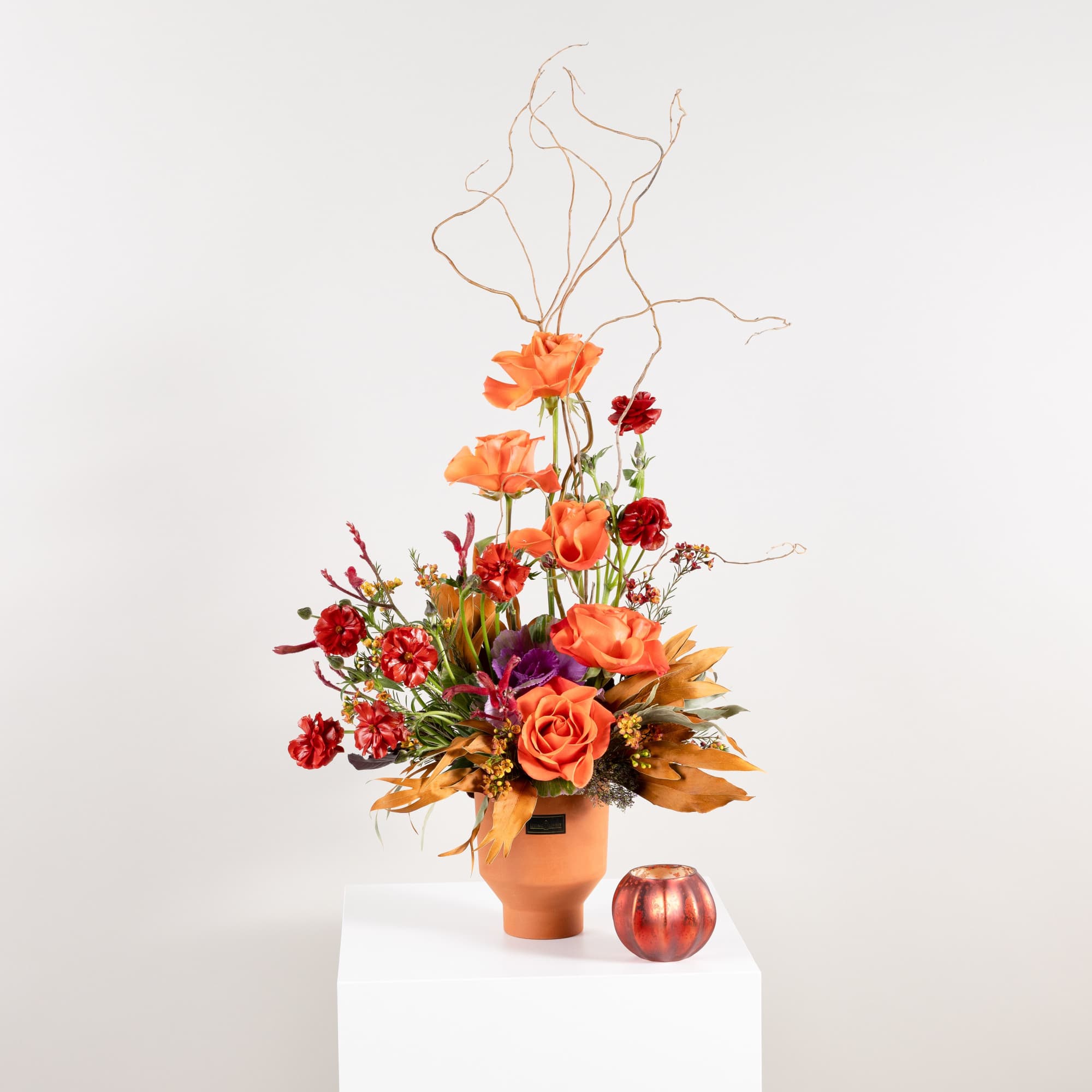 Orange and red floral arrangement in a terracotta vase with curly branches