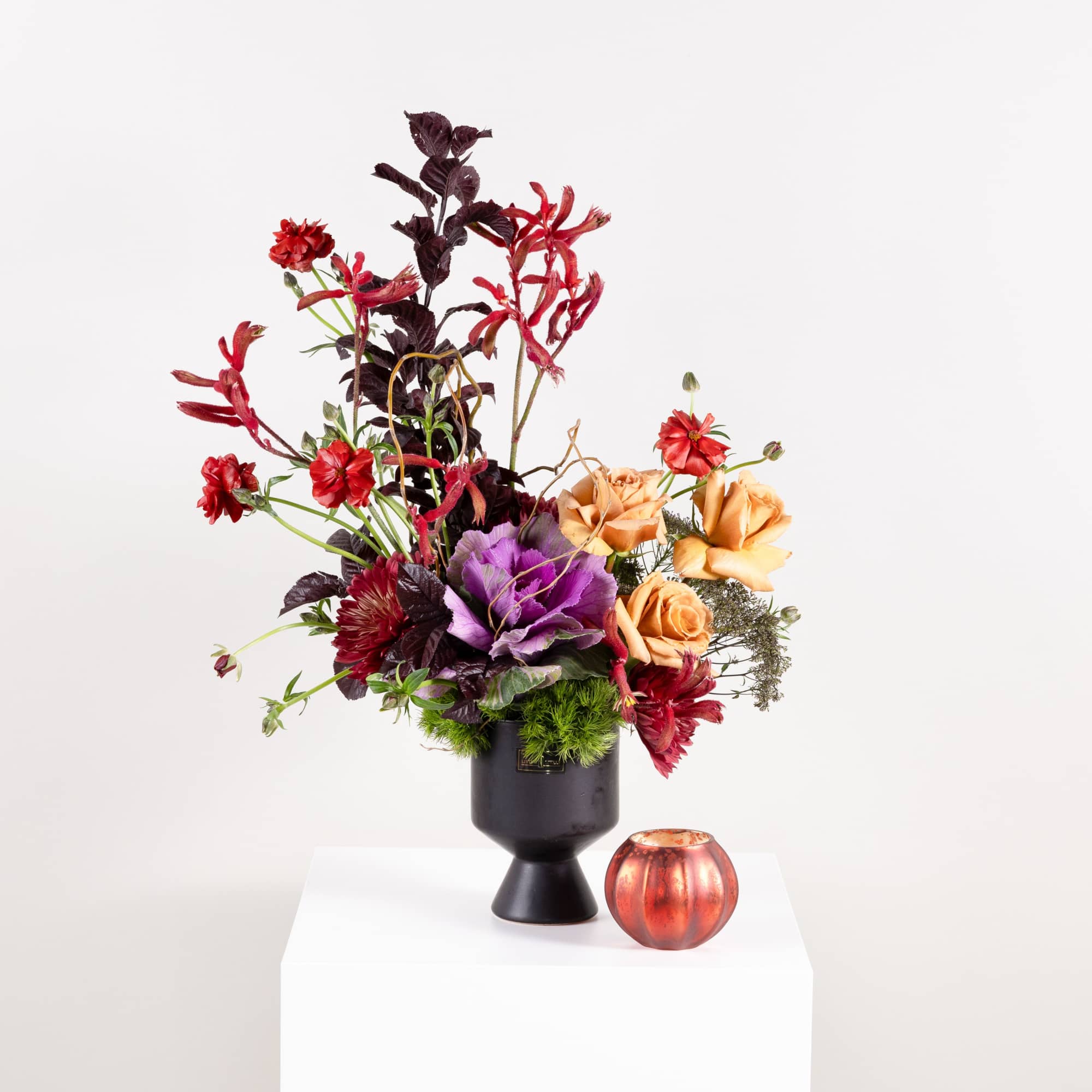 Tall floral arrangement in a black vase with a small orange candle beside it
