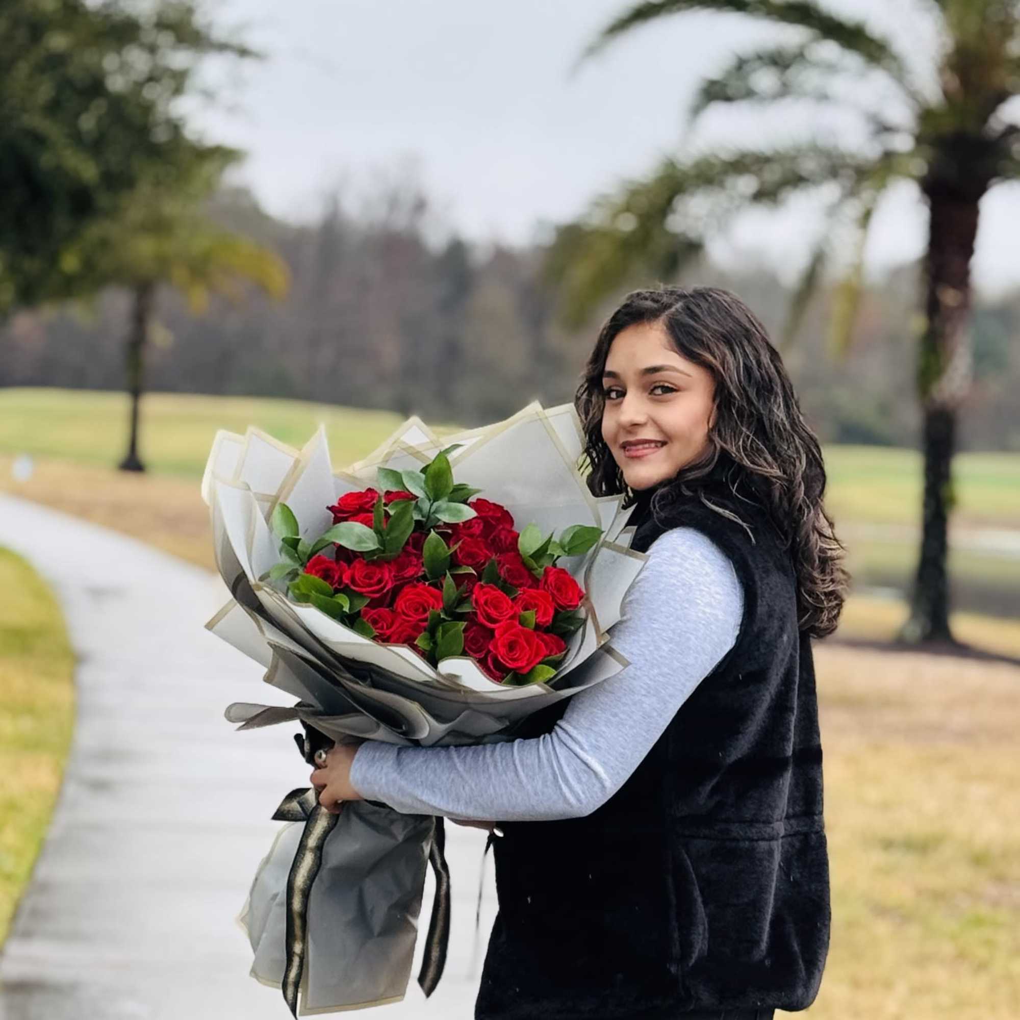 Woman holding a bouquet of red roses wrapped in gray paper