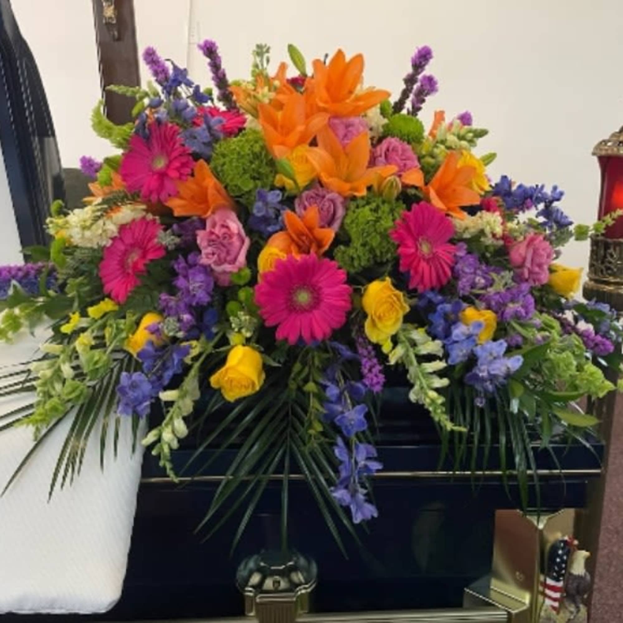 Colorful floral casket spray with orange lilies, pink daisies, and purple blooms