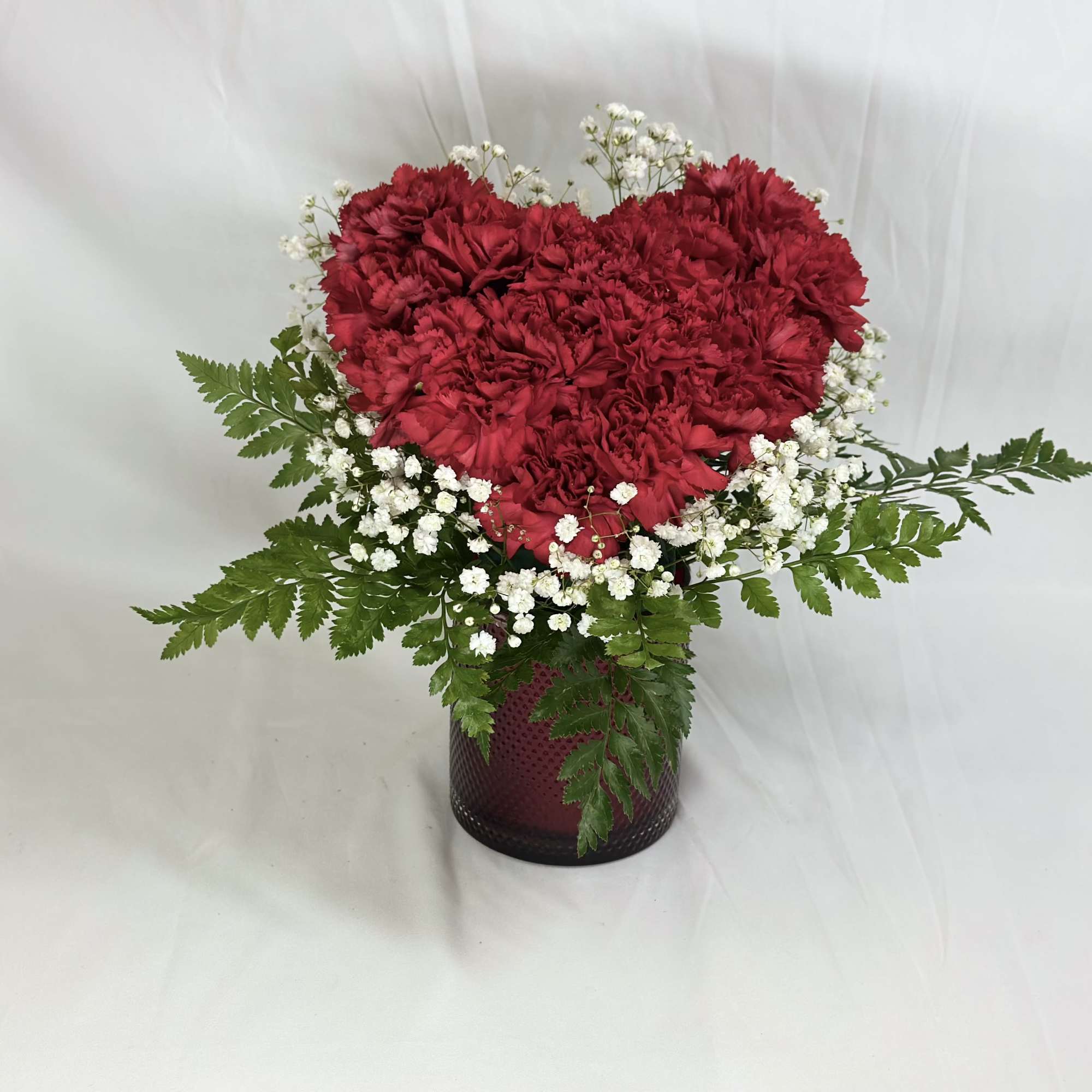 Heart-shaped red carnation arrangement in a dark vase with white baby's breath