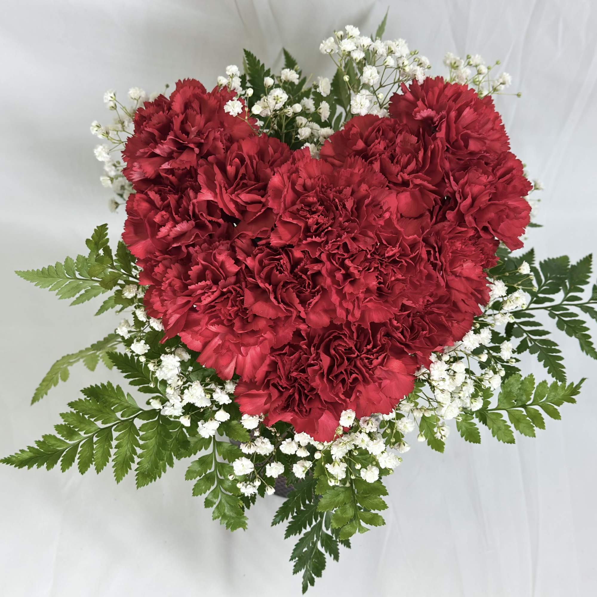 Heart-shaped red carnation arrangement with white baby's breath and fern foliage