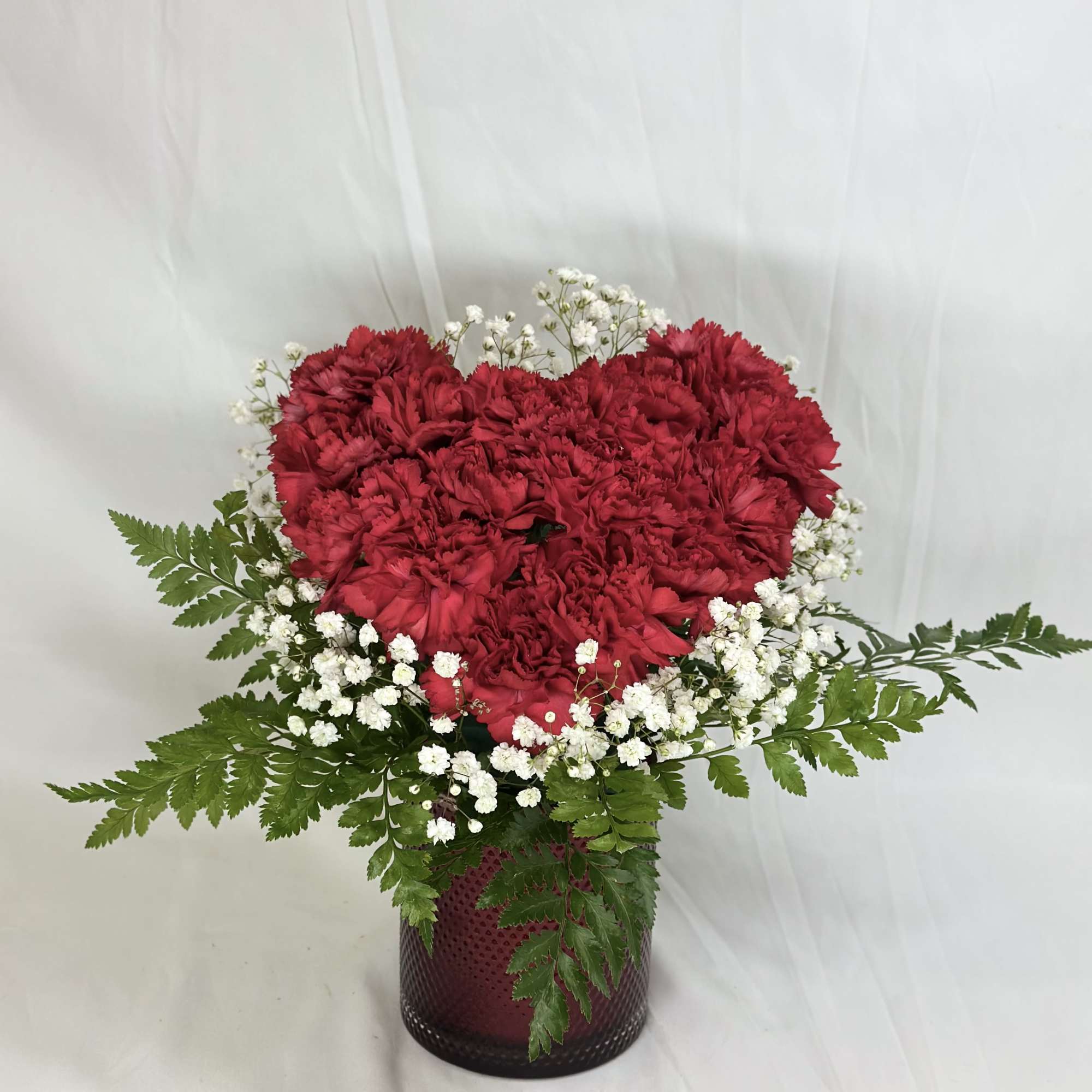 Red carnation arrangement in a dark glass vase with white baby's breath