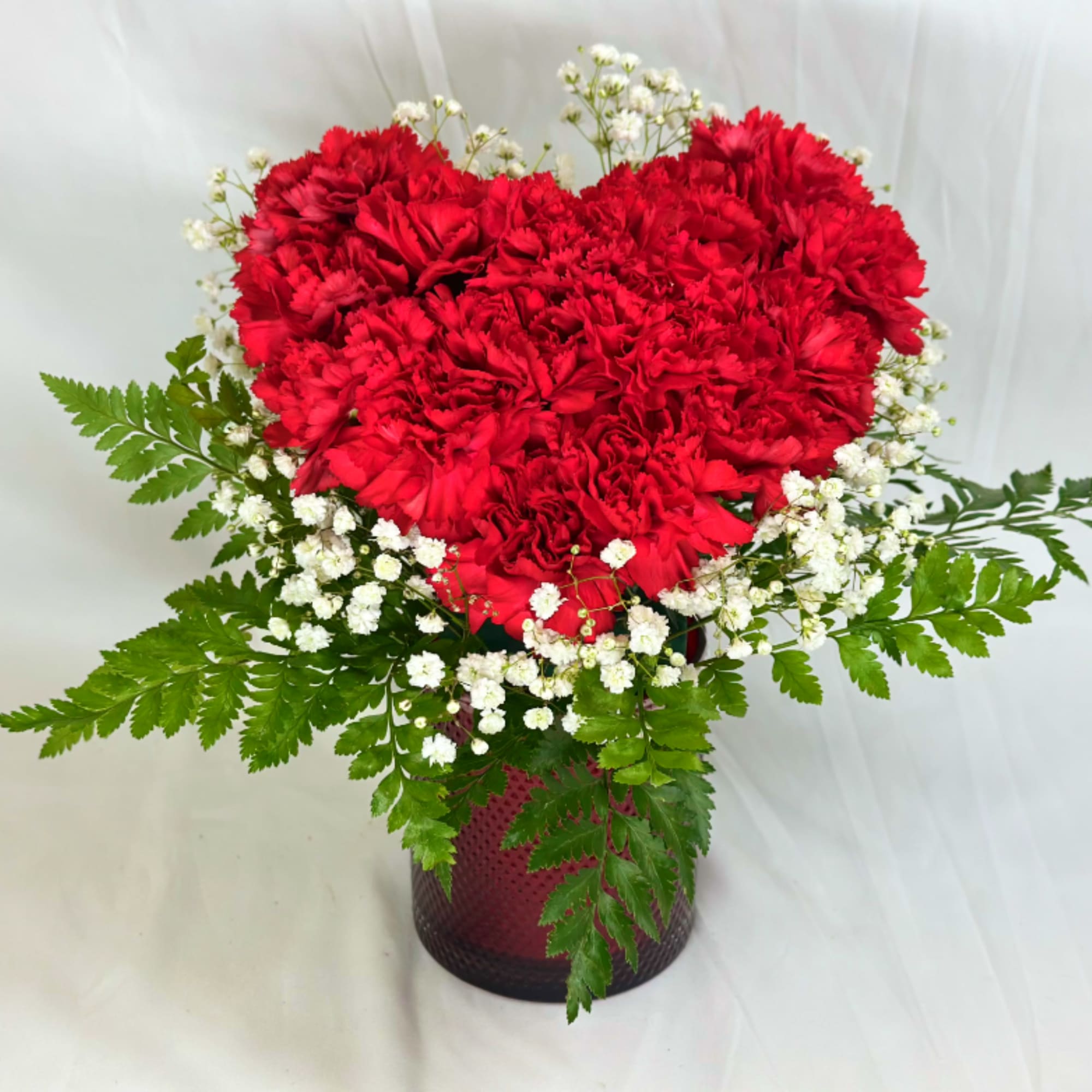 Heart-shaped red carnation arrangement with white baby's breath in a vase