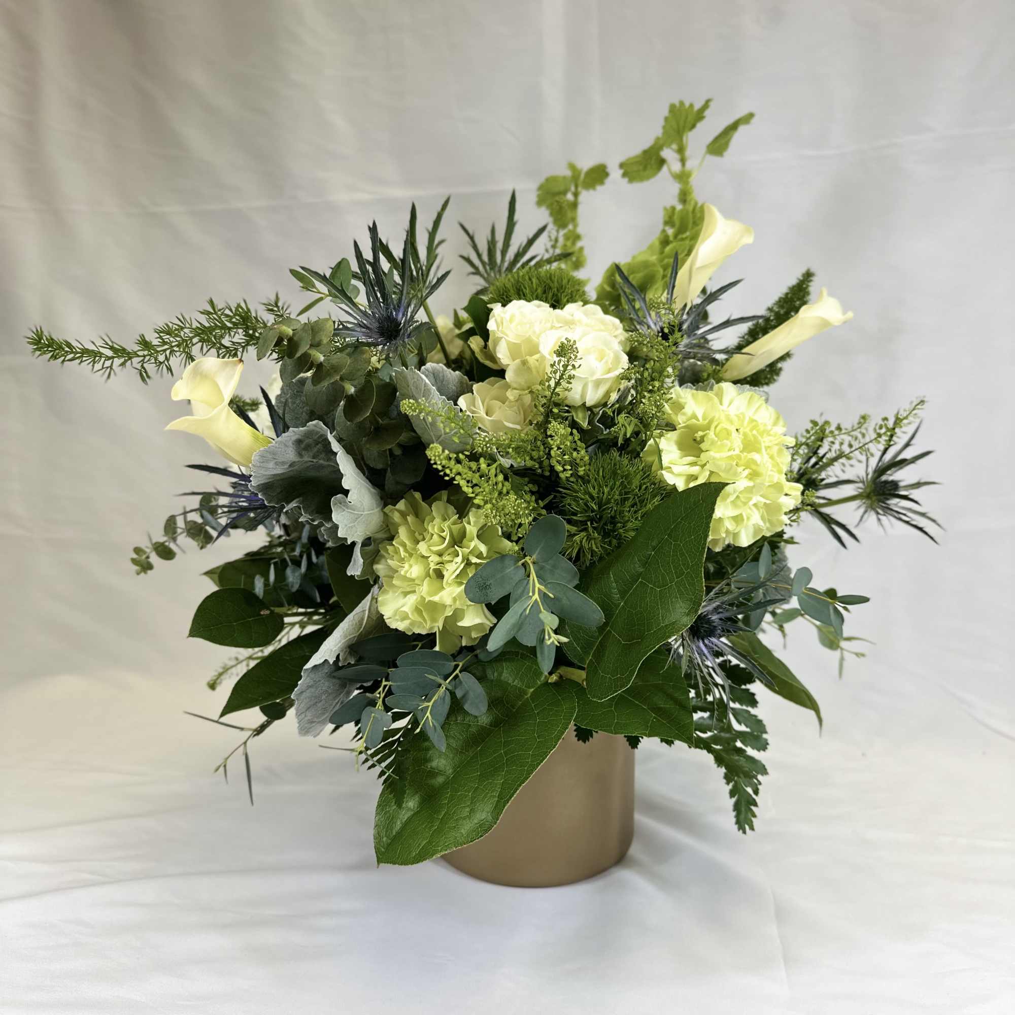 Green and white floral arrangement in a gold vase