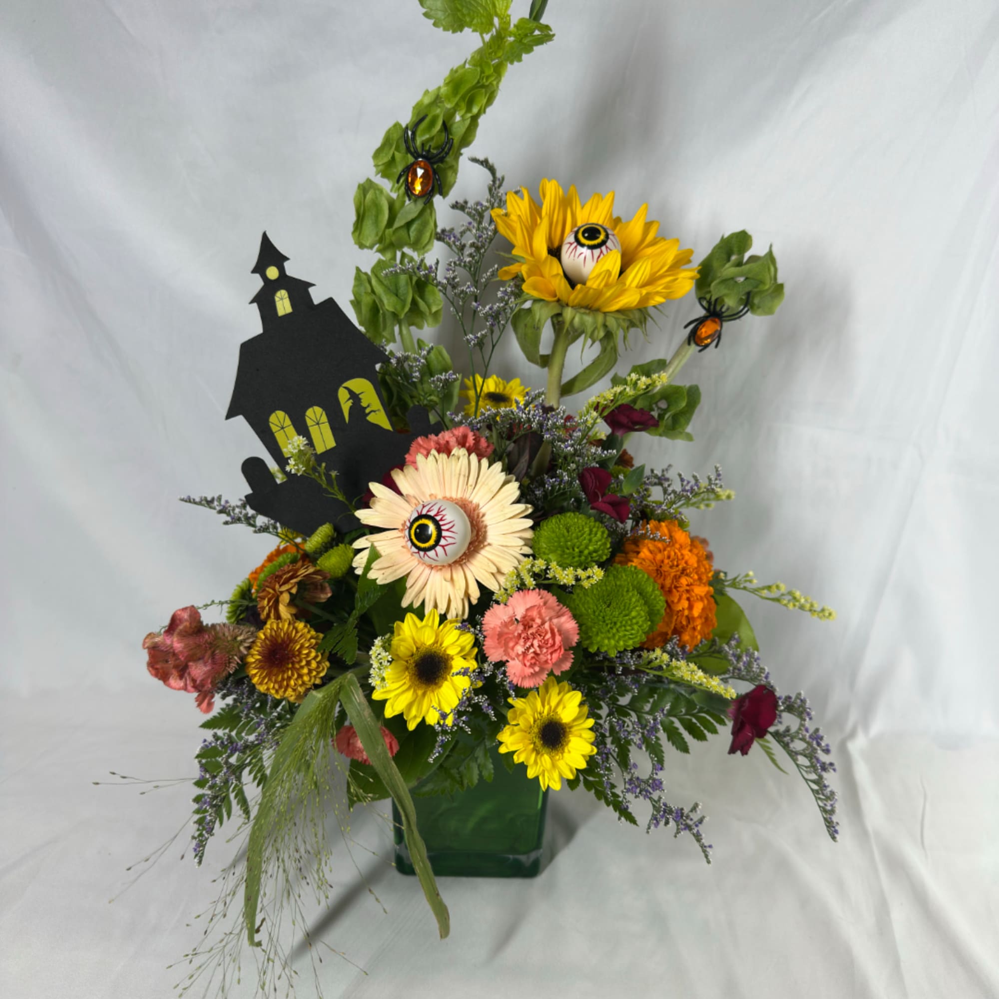 Halloween floral arrangement with sunflowers, mums, and eyeball picks in a green vase