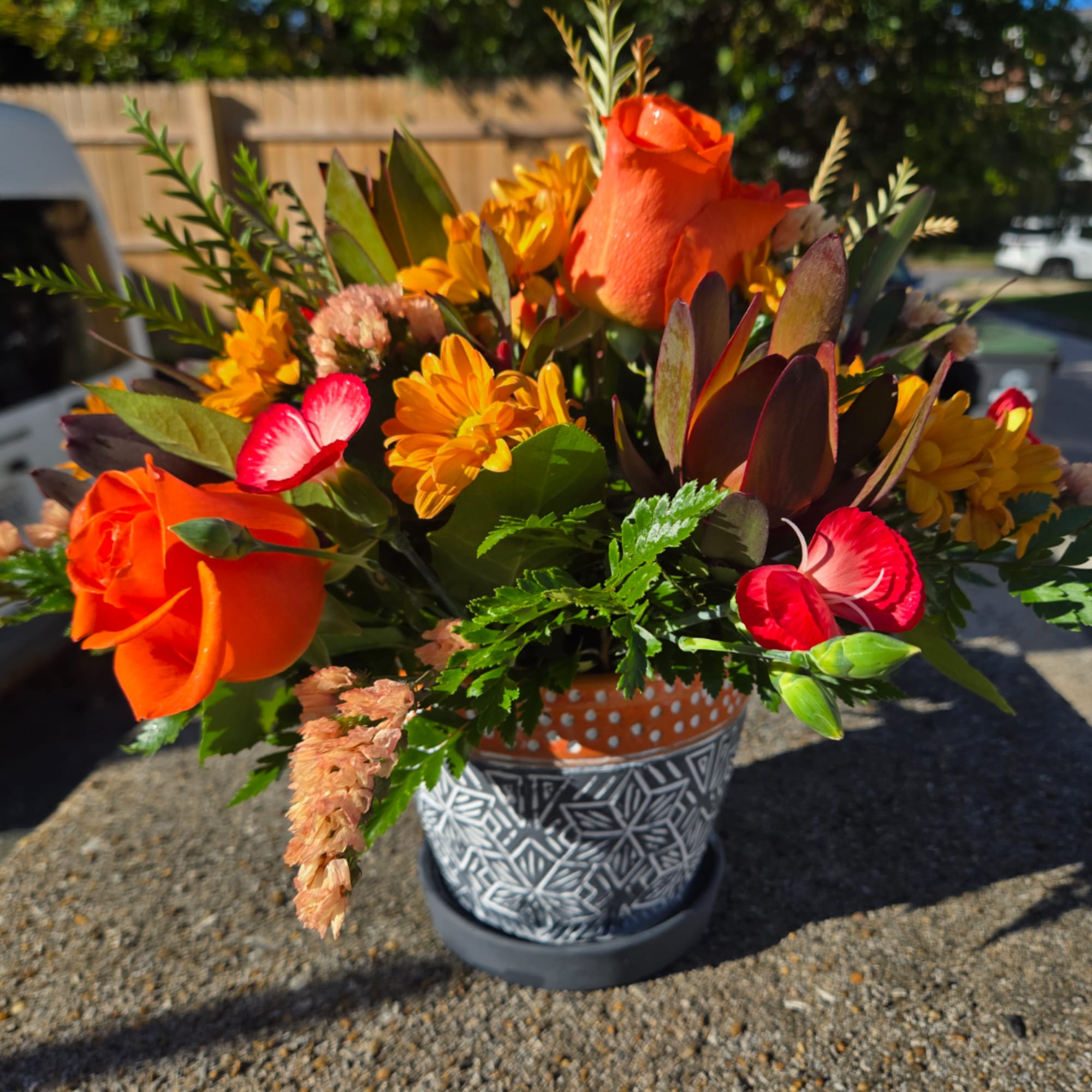 Orange roses and yellow flowers in a patterned pot outdoors