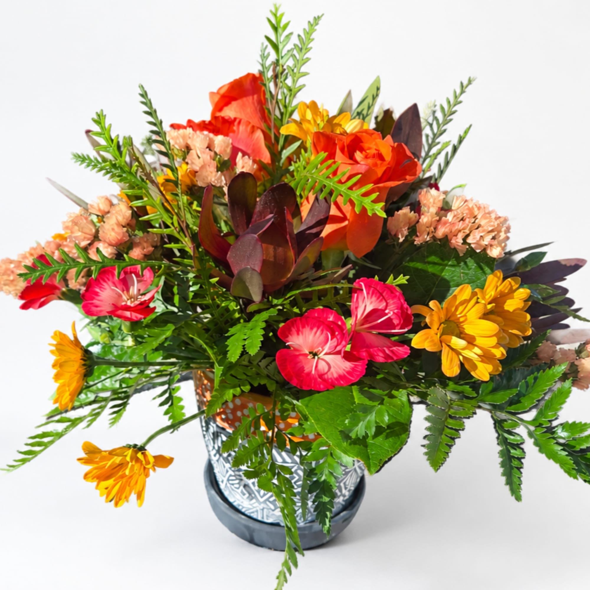 Bright mixed bouquet in a patterned glass vase with orange, pink, and yellow flowers