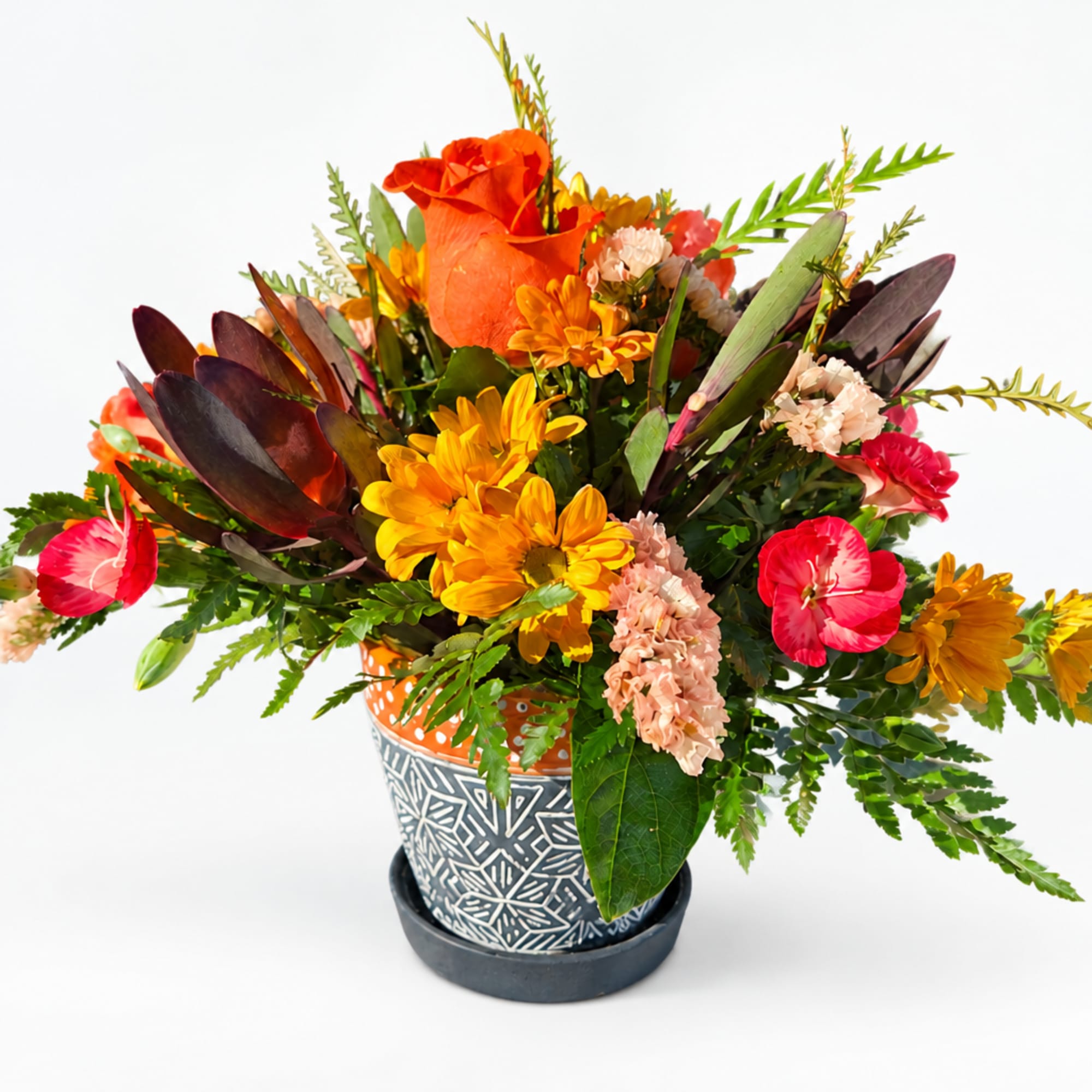 Bright mixed flower arrangement in a patterned pot with orange and yellow blooms