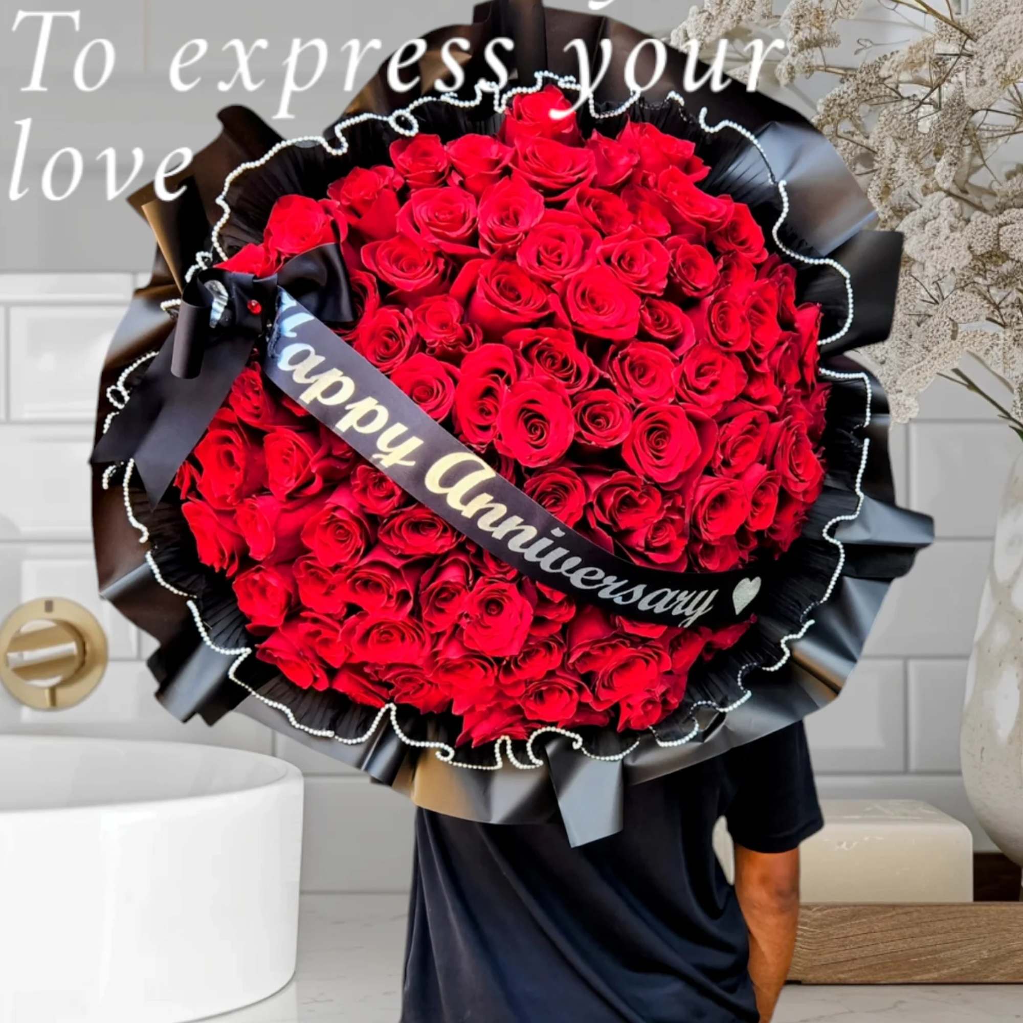 Large bouquet of red roses wrapped in black paper with a "Happy Anniversary" ribbon