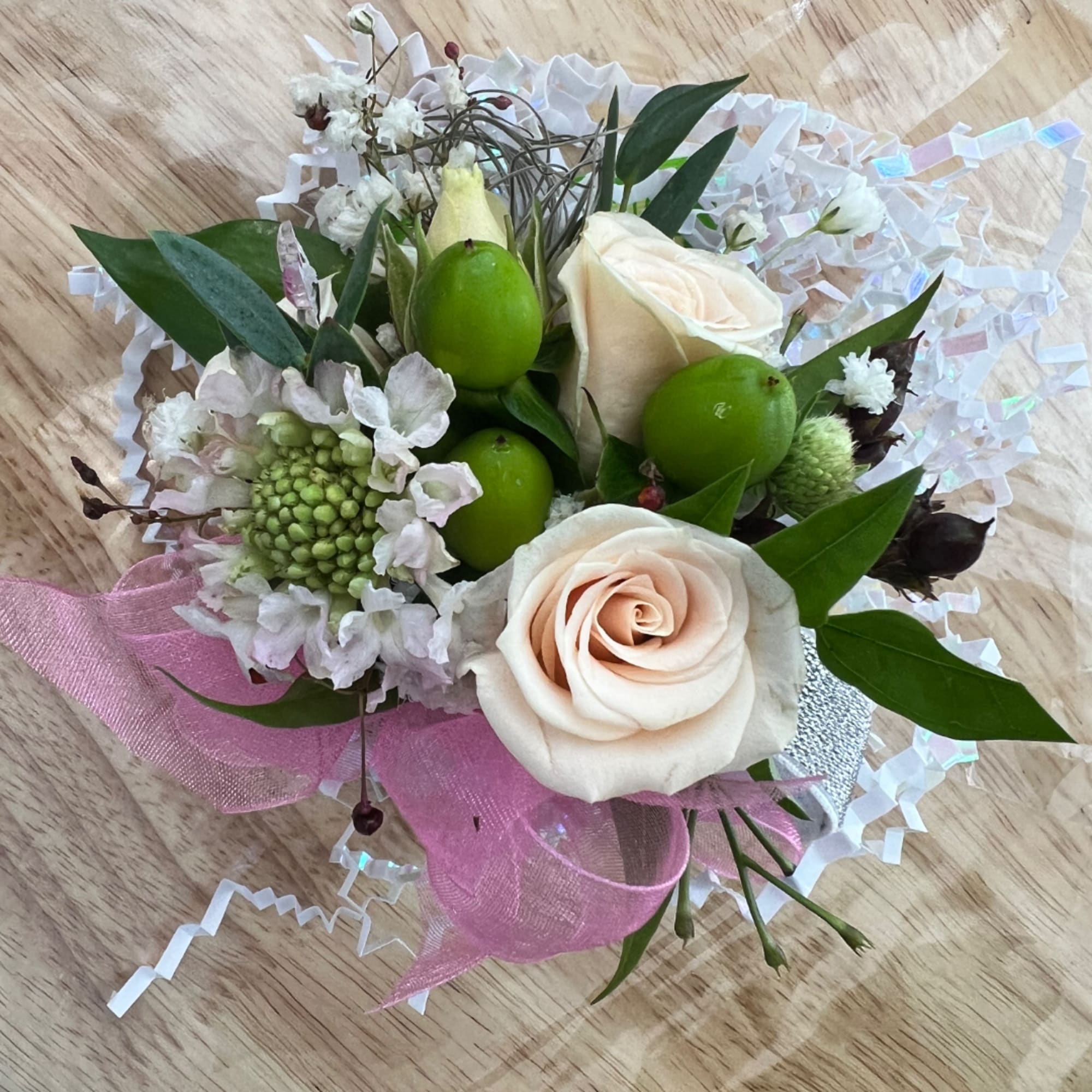 Small bouquet of cream roses and white flowers with green berries and pink ribbon
