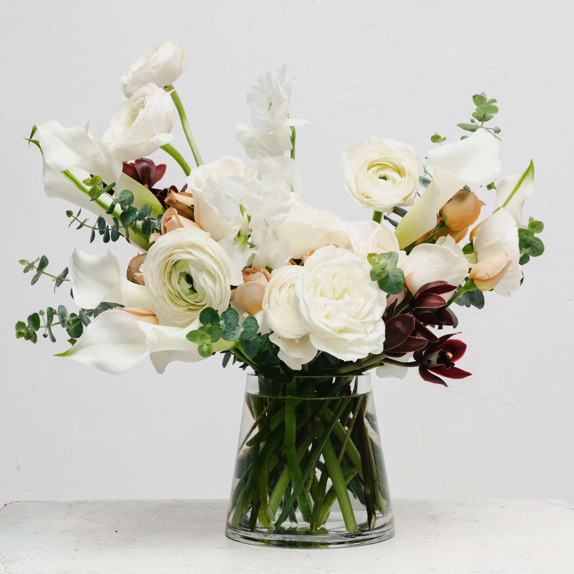 White floral arrangement in a clear glass vase with calla lilies and ranunculus