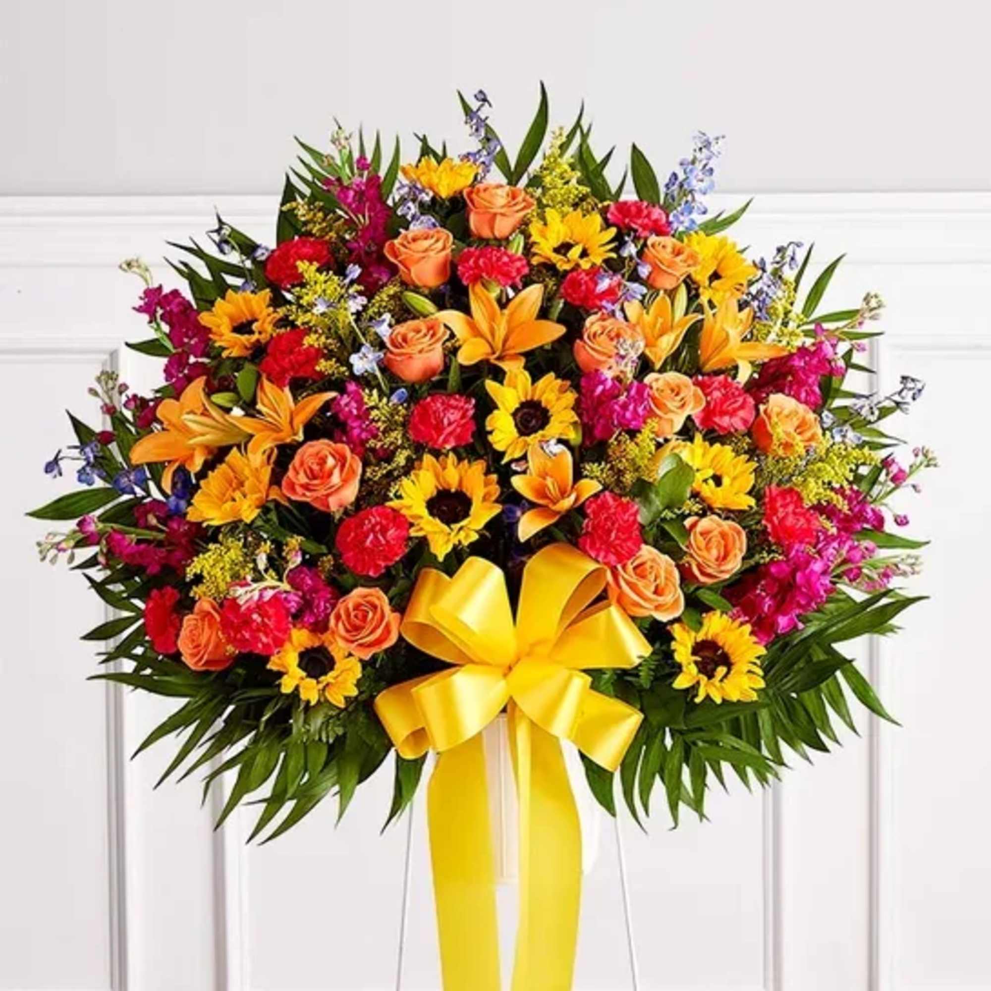 Standing spray of mixed flowers with a yellow ribbon on an easel