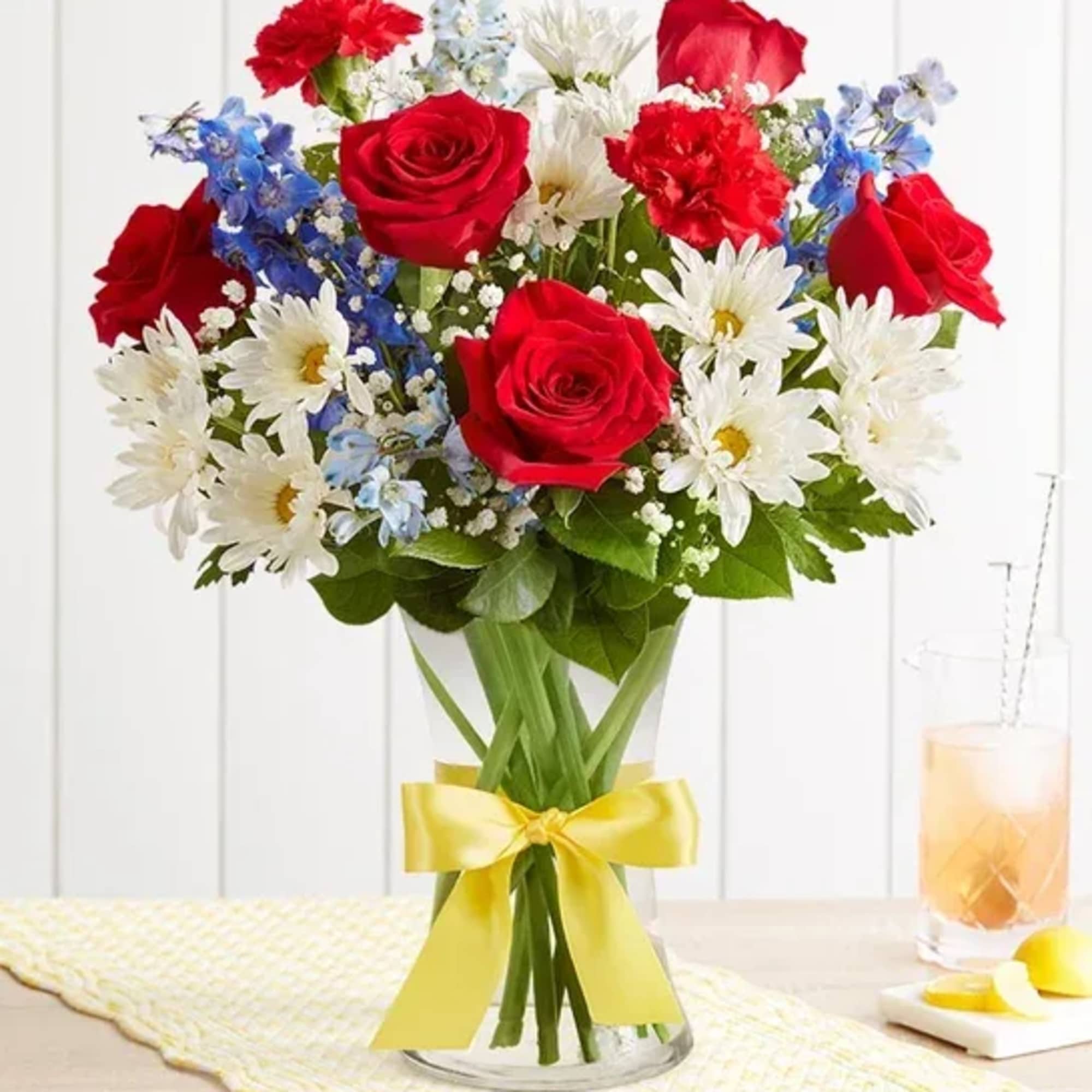 Bouquet of red roses, white daisies, and blue flowers in a glass vase