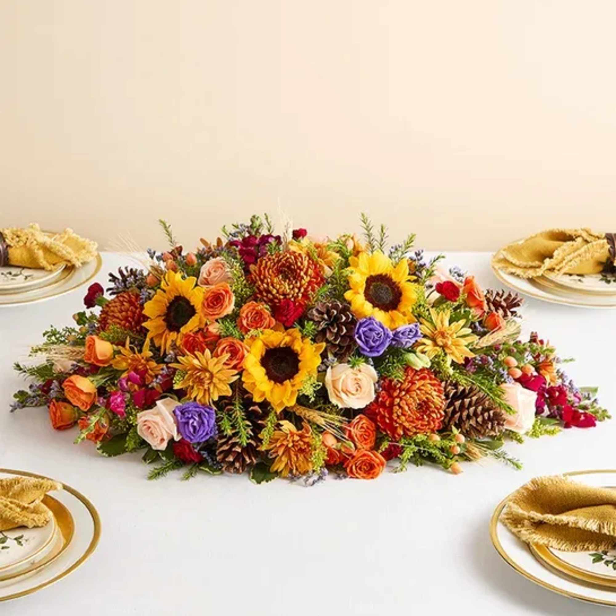 Low floral centerpiece with sunflowers, roses, and pinecones on a table
