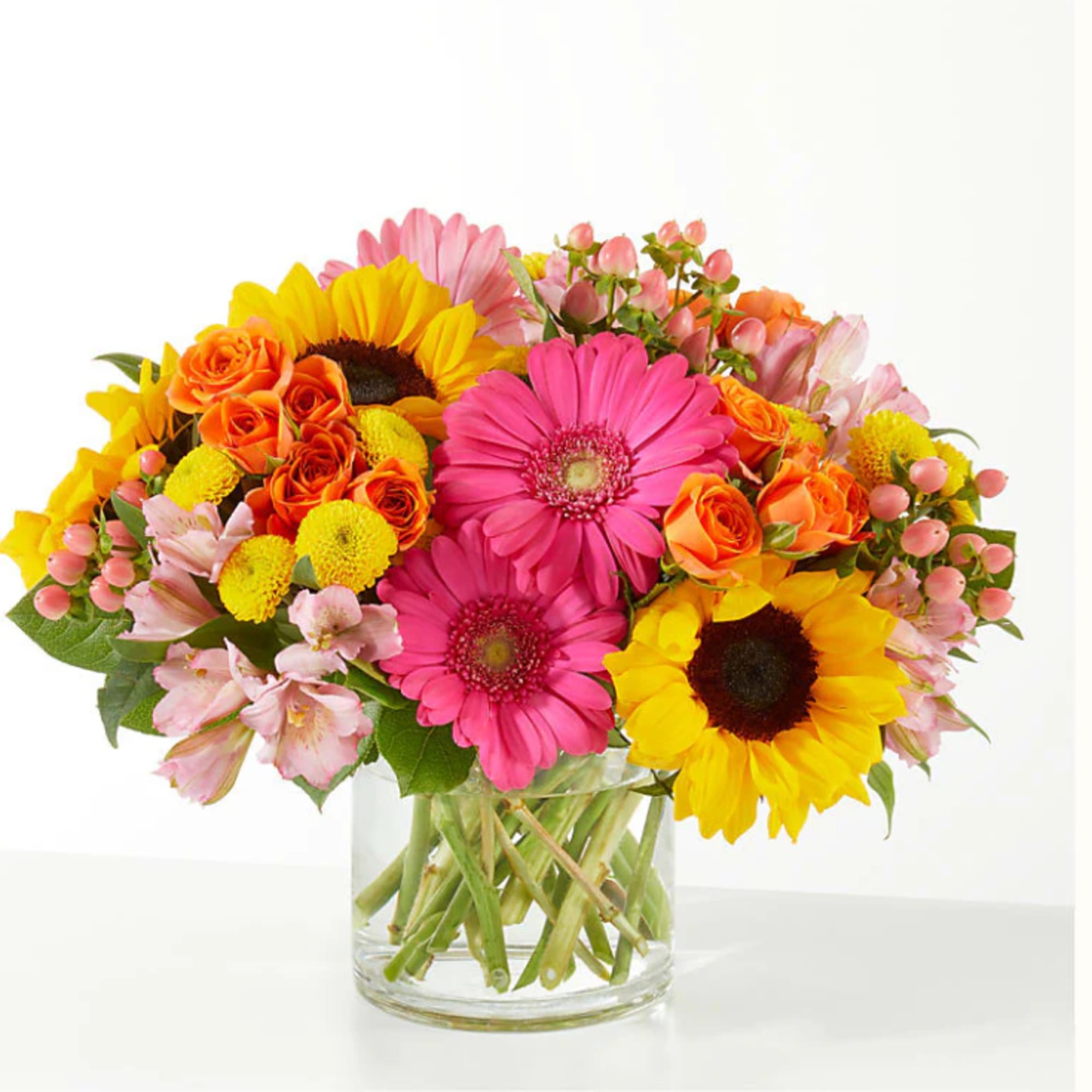 Bright mixed bouquet of gerbera daisies, sunflowers, roses, and alstroemeria in a glass vase