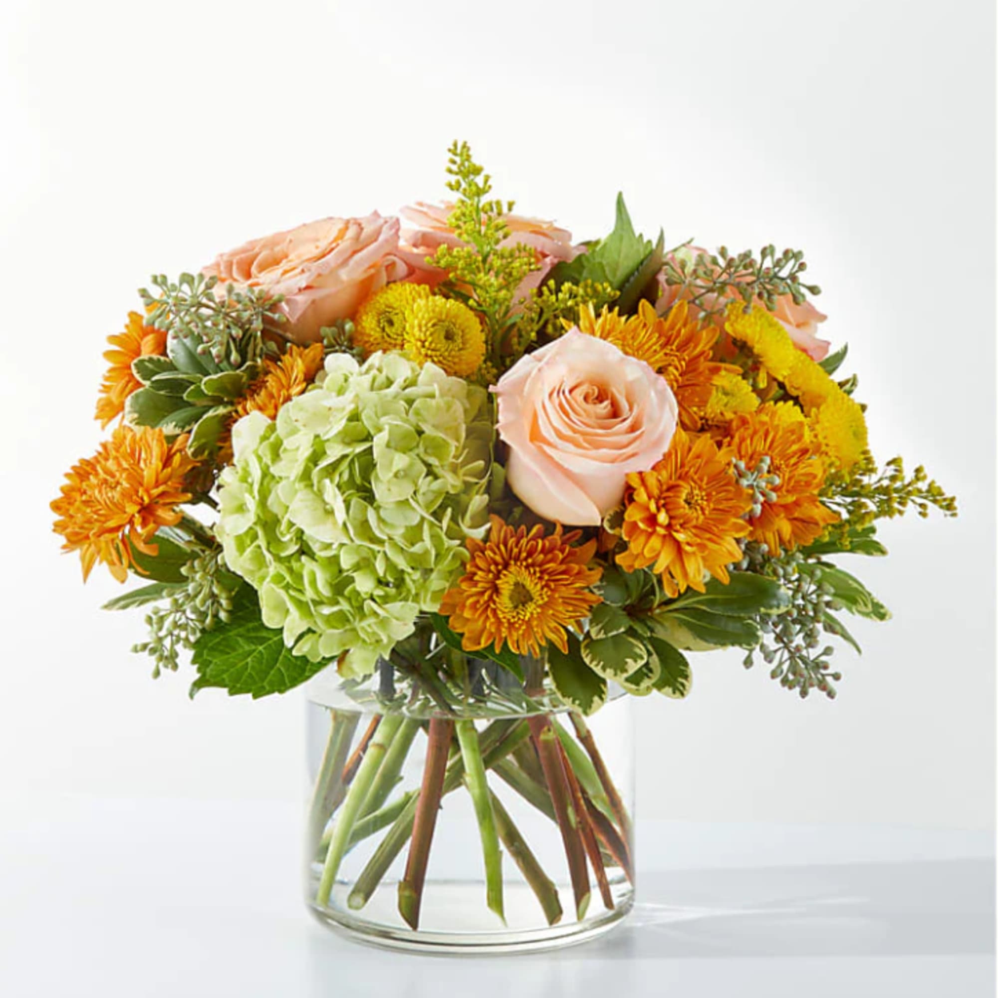 Peach roses and orange mums in a clear glass vase with green hydrangea