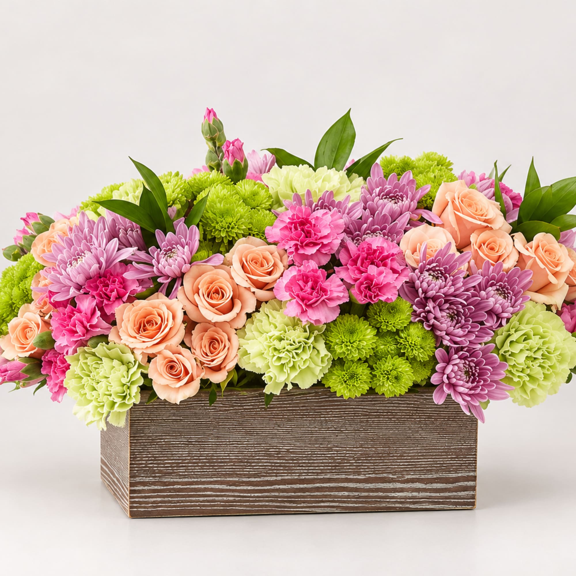 Mixed bouquet of pink, peach, and green flowers in a wooden box