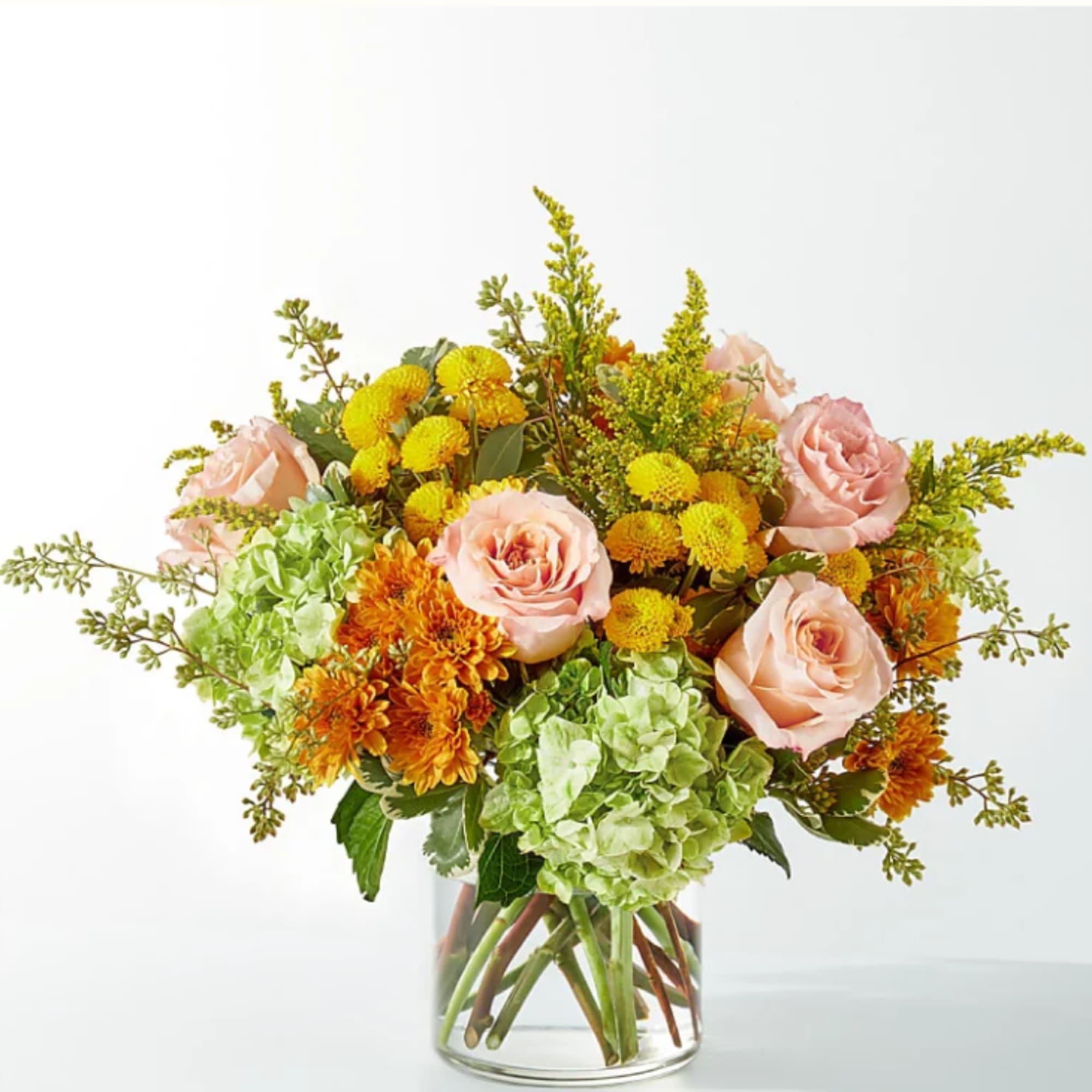 Bouquet of peach roses, green hydrangea, and yellow-orange mums in a glass vase