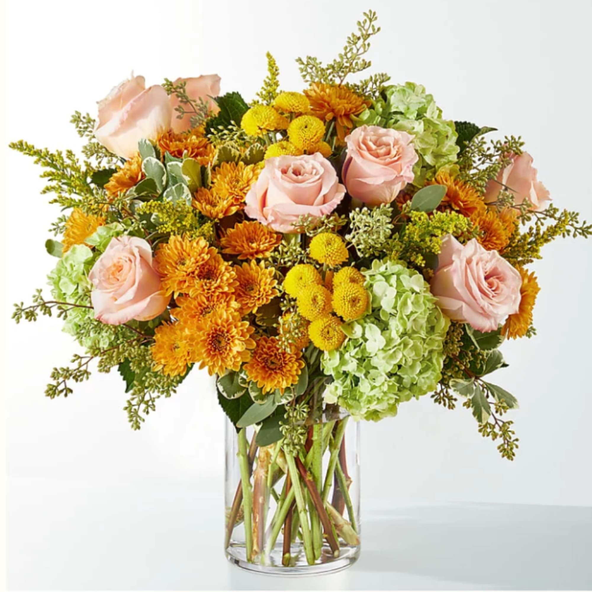 Bouquet of pink roses, orange mums, and green hydrangeas in a clear glass vase