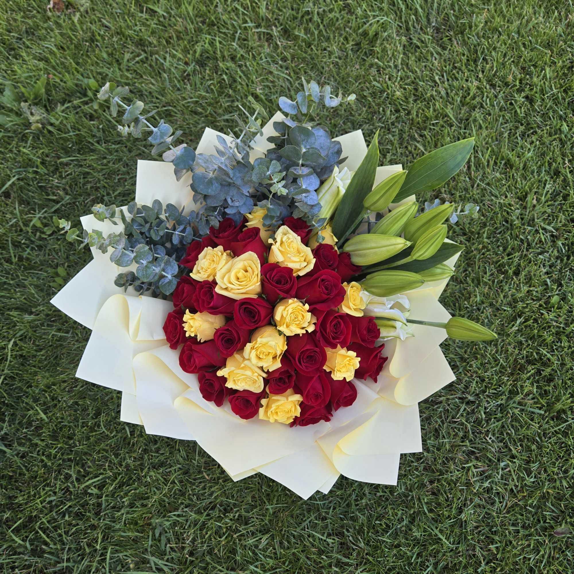 Bouquet of red and yellow roses with lilies and eucalyptus on white wrap
