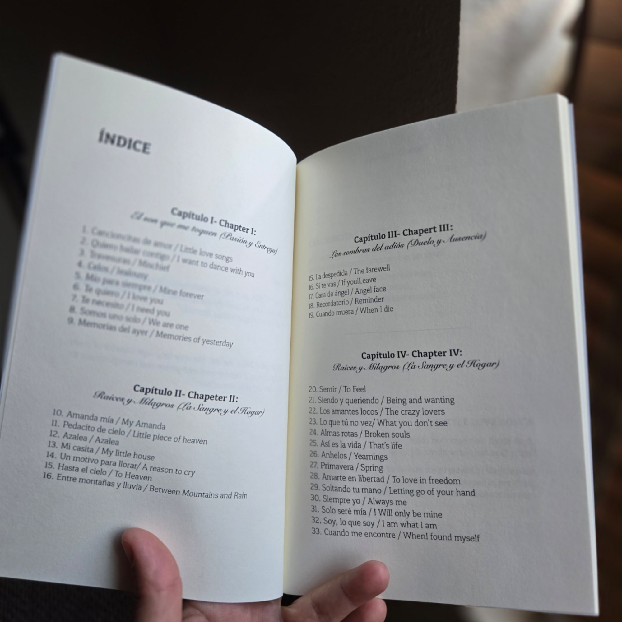 Open book showing a Spanish-English table of contents, held by two hands