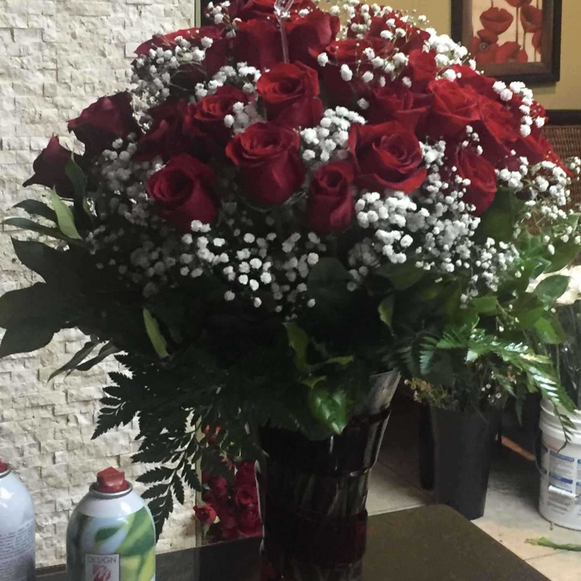 Large bouquet of red roses and white filler flowers in a tall dark glass vase