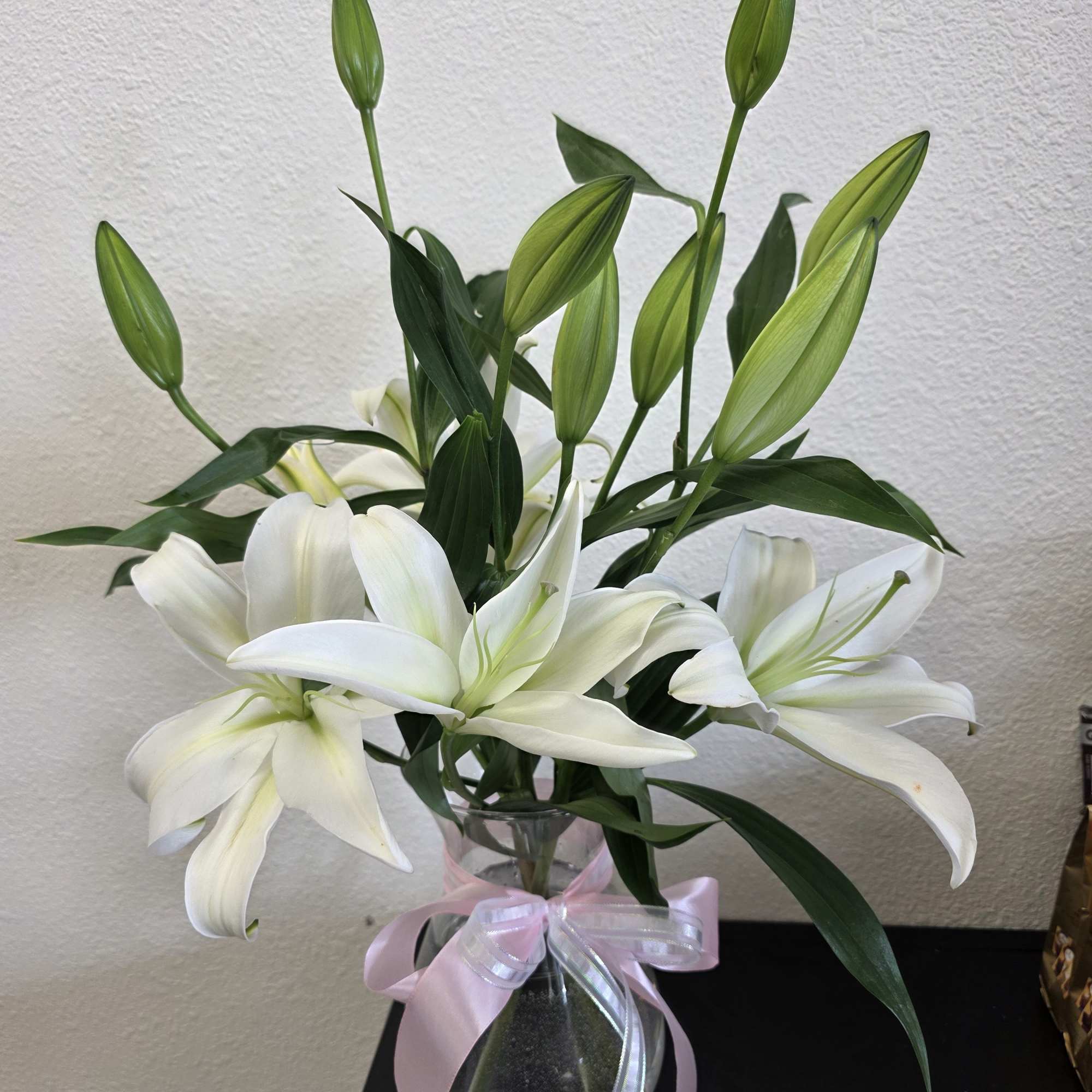 White lilies in a clear glass vase with a pink ribbon