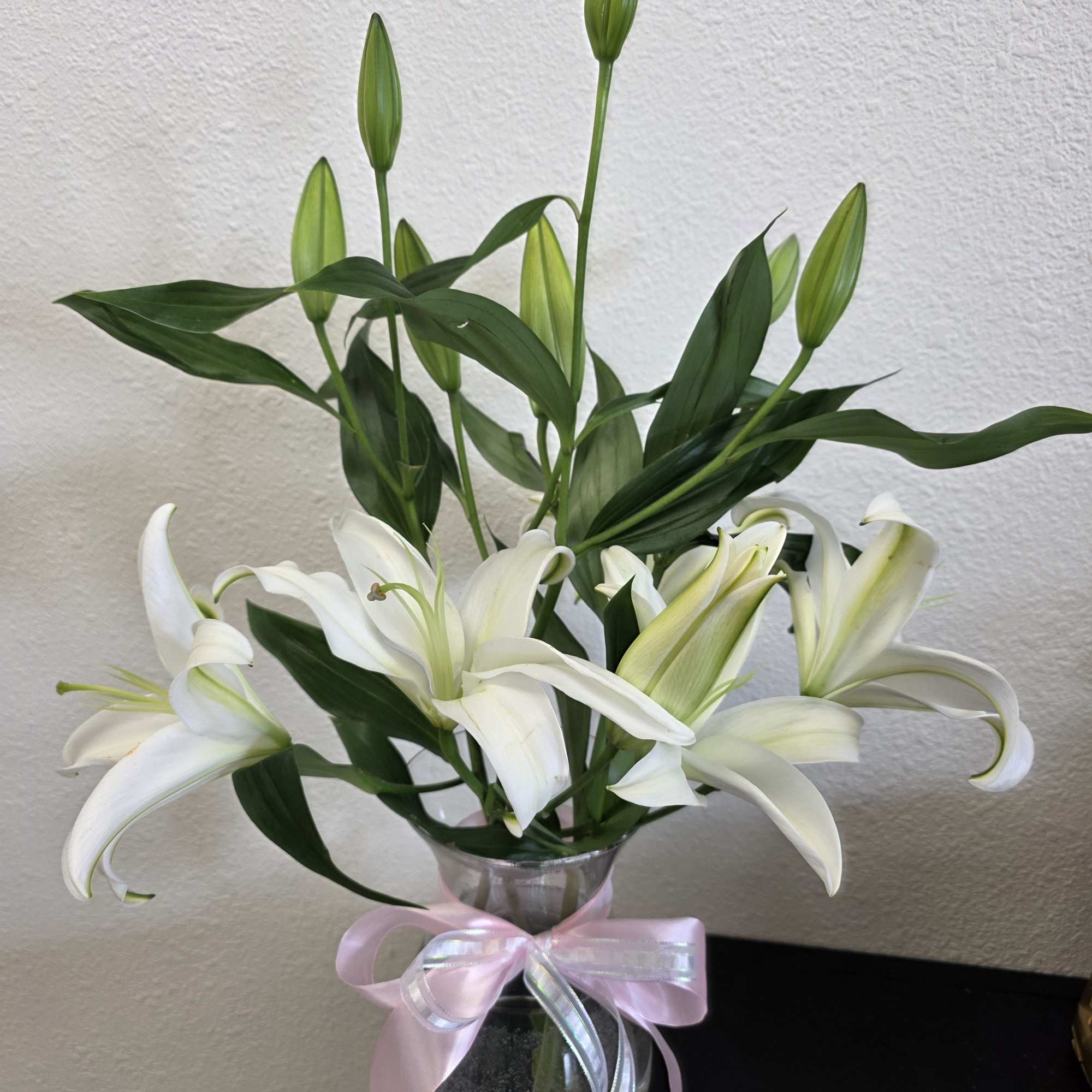 White lilies in a clear glass vase with a pink ribbon