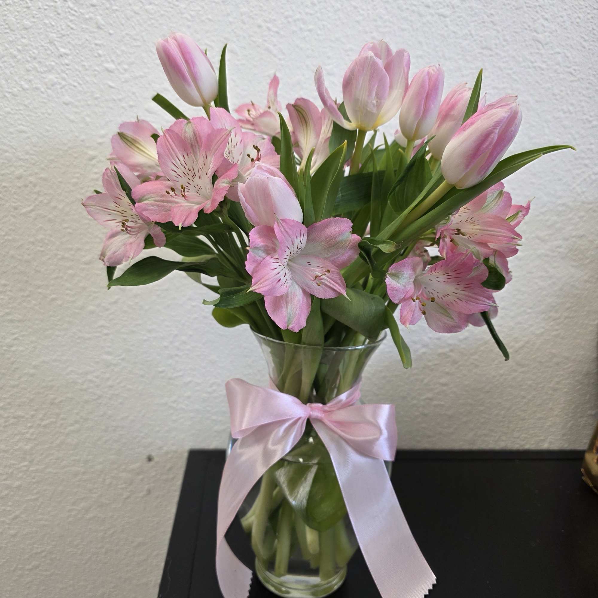 Pink tulips and alstroemeria in a clear glass vase with a pink ribbon