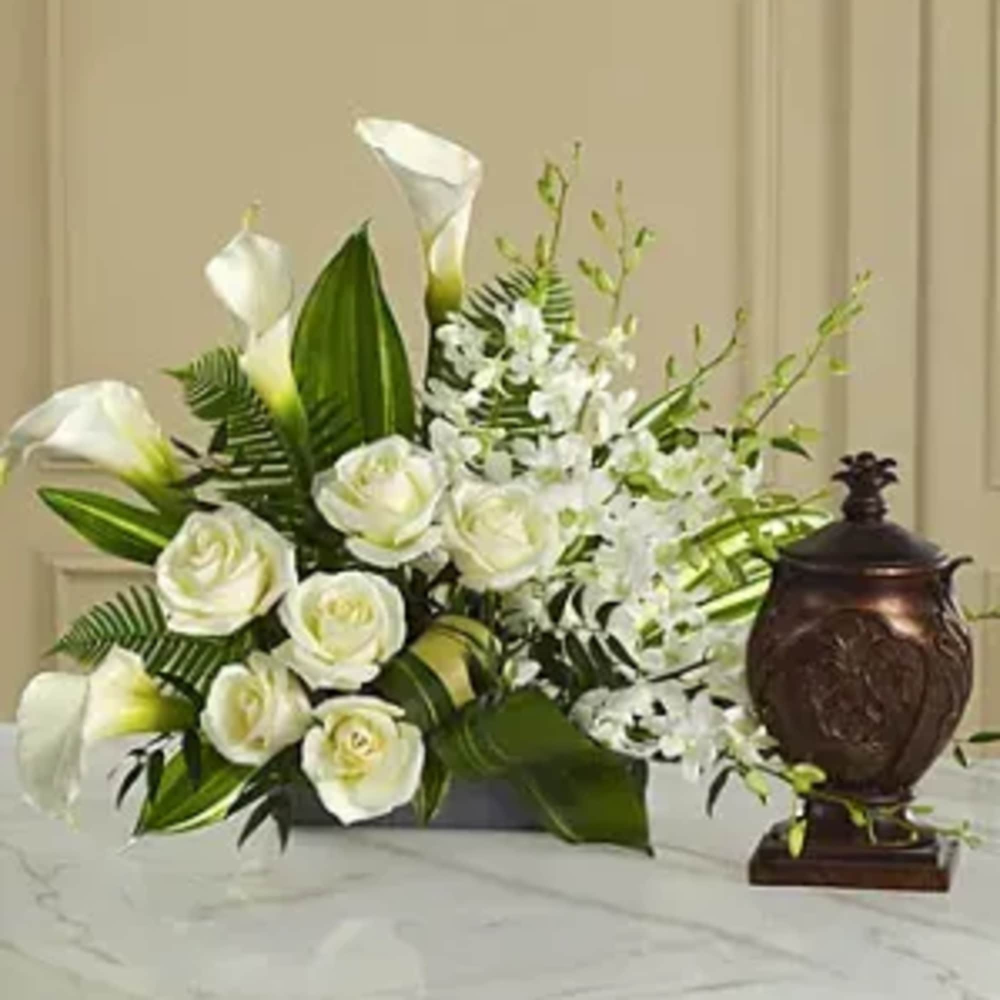 White roses and calla lilies arranged with white orchids in a low container