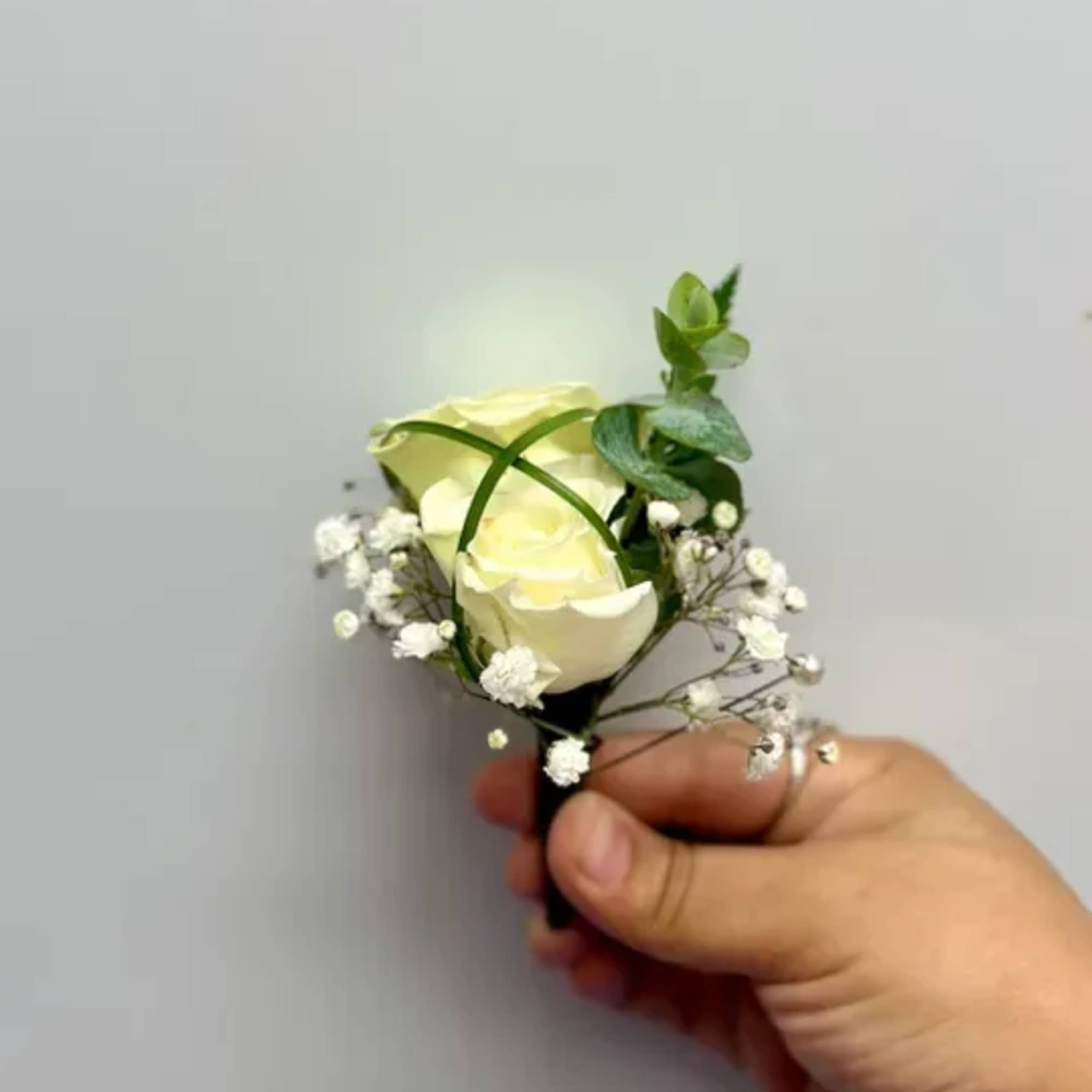 Small white rose boutonniere with baby's breath and greenery, photo 2 of 2