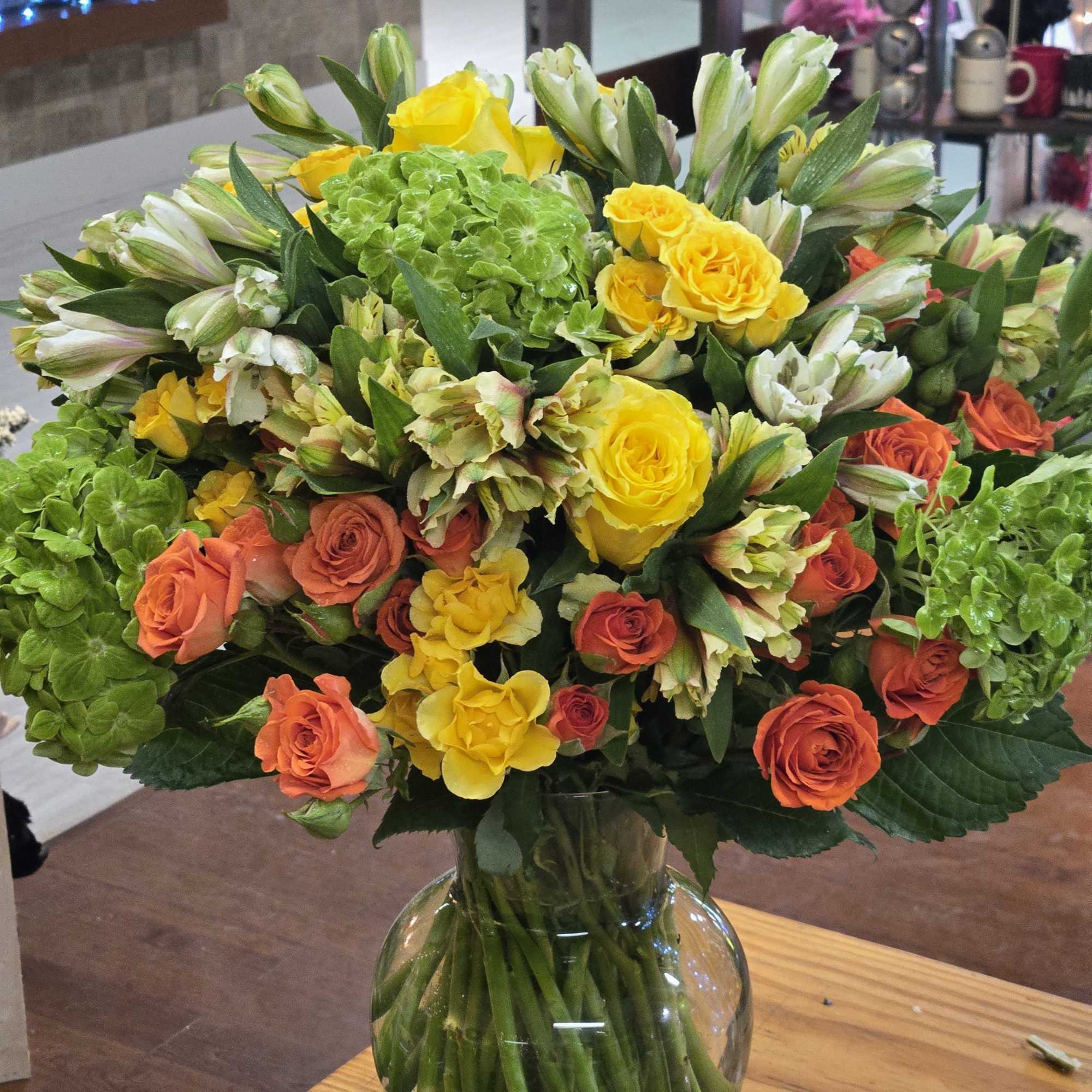 Bouquet of yellow and orange roses with green hydrangeas in a glass vase