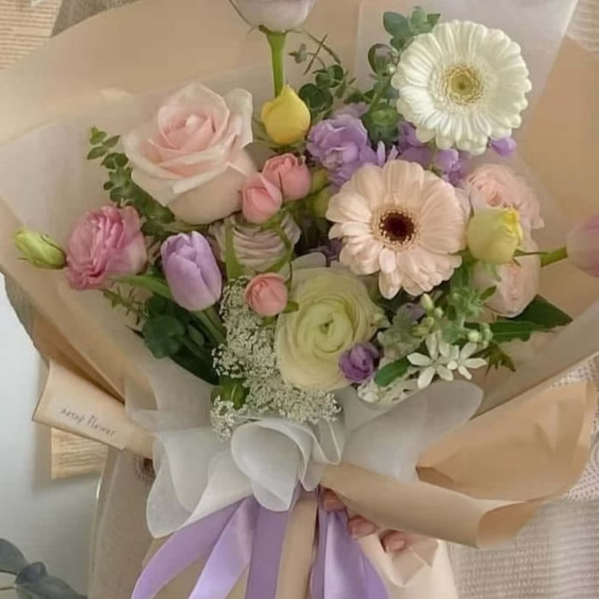 Pastel bouquet with roses, tulips, and gerbera daisies wrapped in beige paper