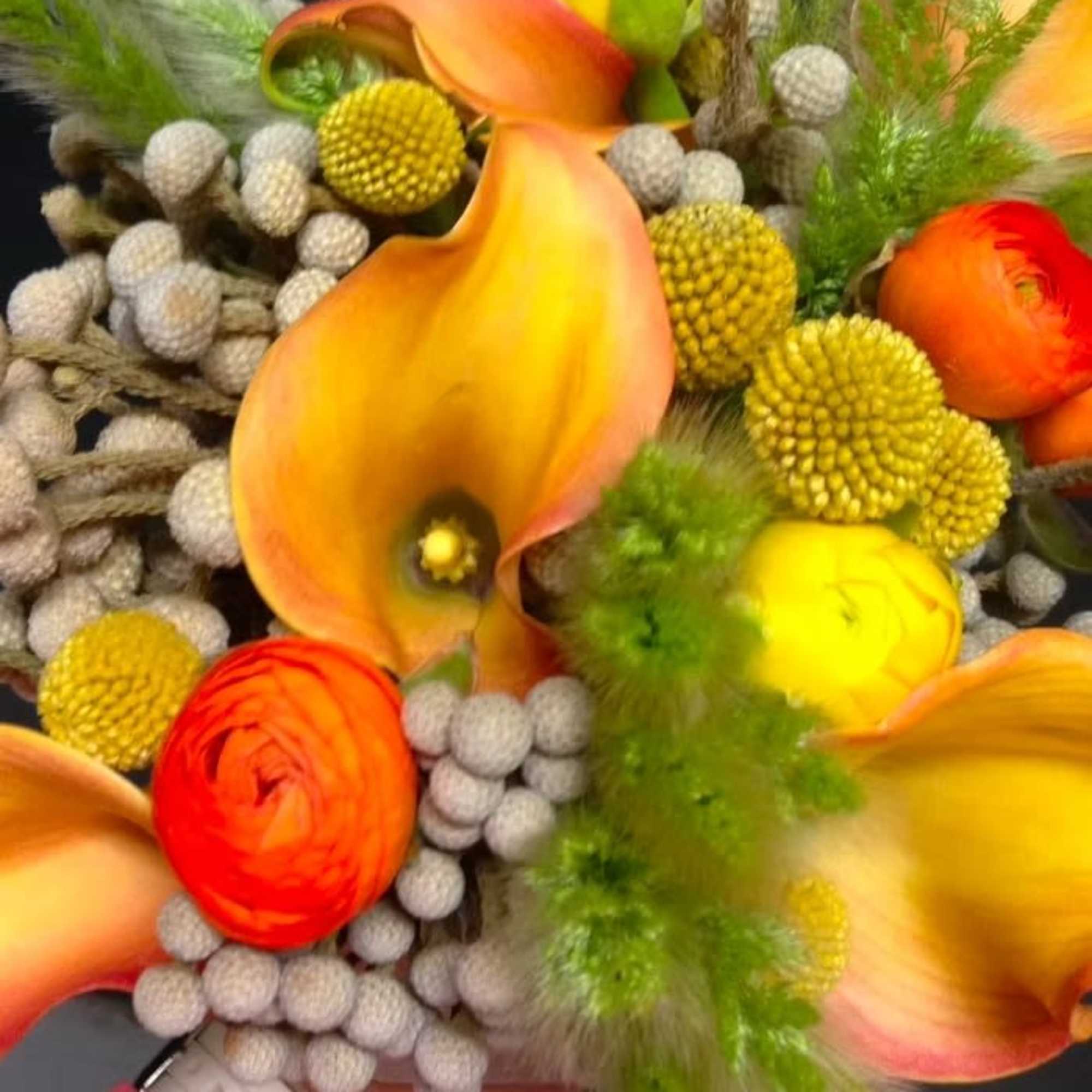 Bouquet of orange calla lilies and yellow ranunculus with textured seed pods