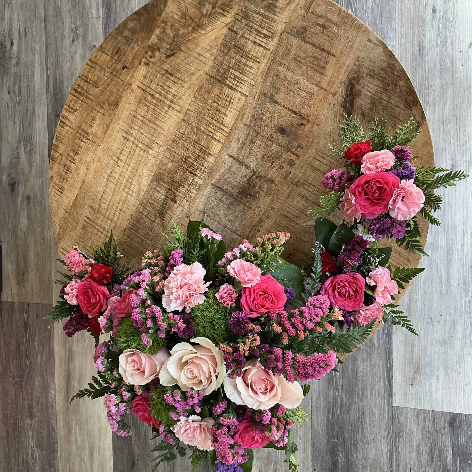 Heart-shaped floral arrangement with pink and purple roses on a wooden table