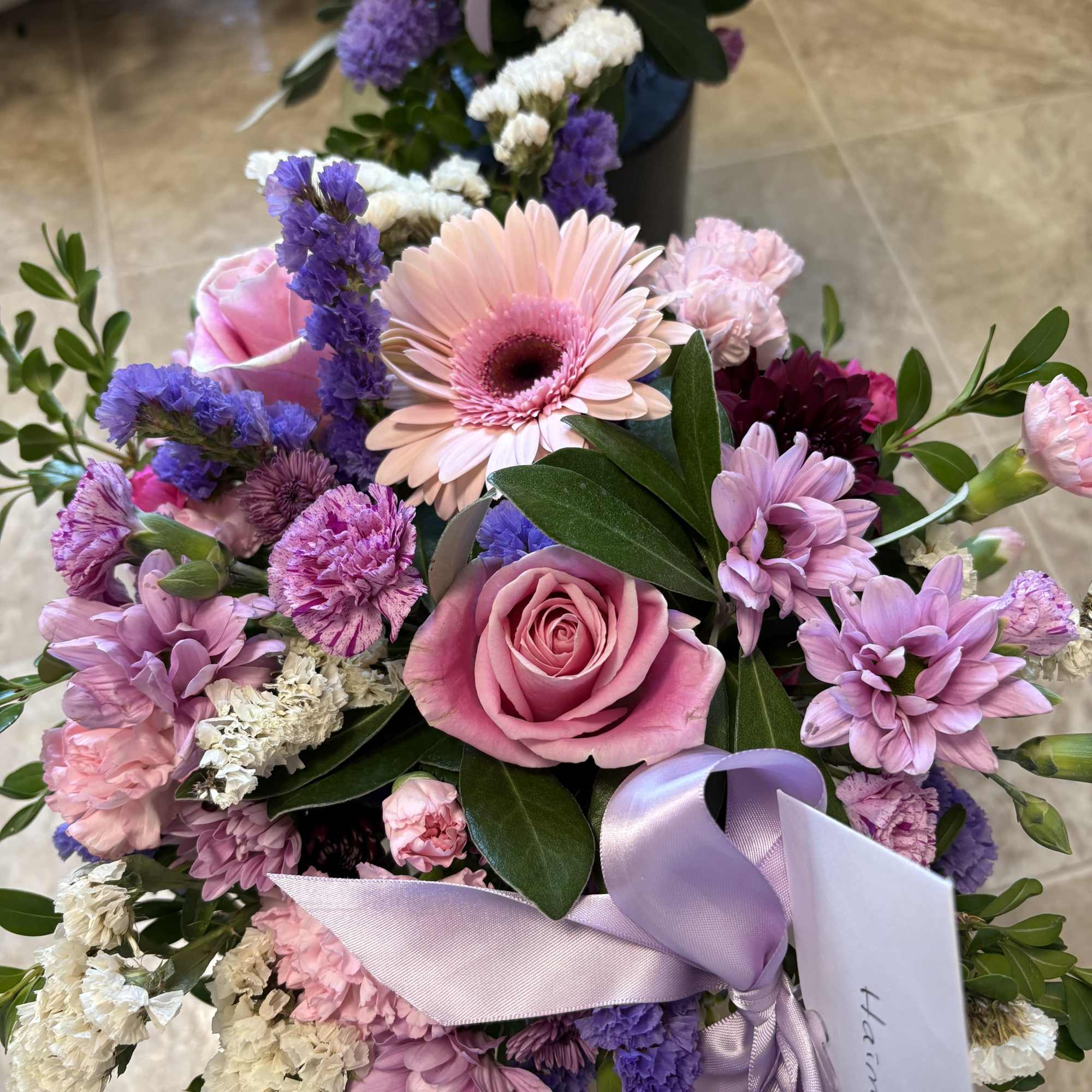 This arrangement has greenery, different types of season, flowers, pink and purple