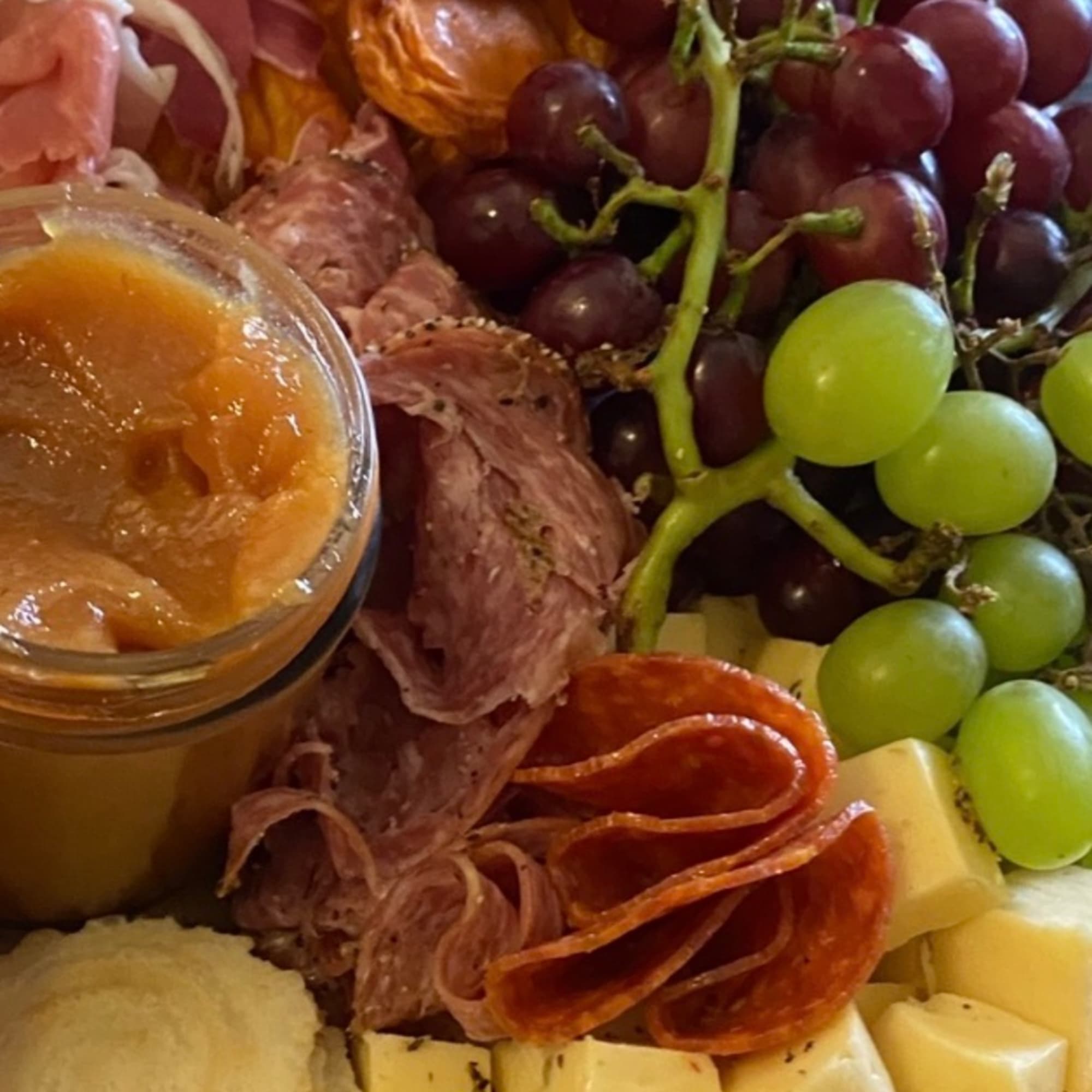 Charcuterie board with grapes, cheese, cured meat, and a jar of spread
