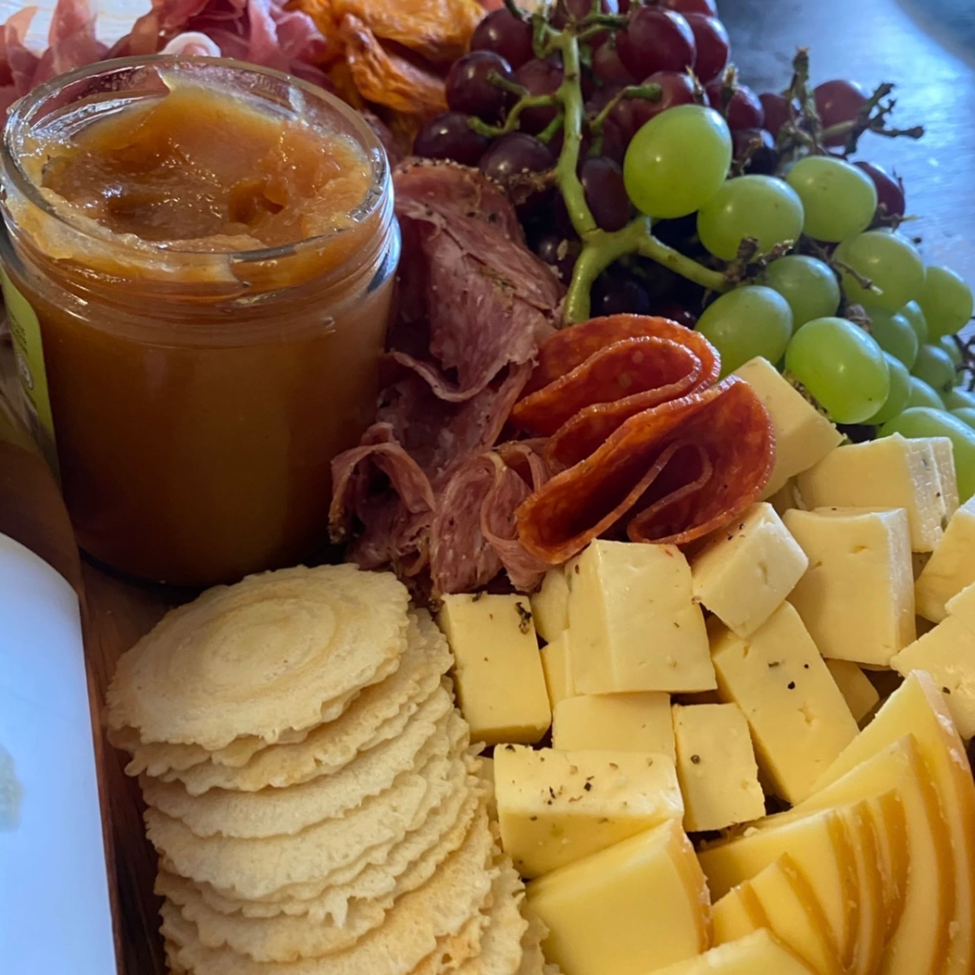 Charcuterie board with grapes, cheese cubes, crackers, cured meat, and a jar of spread