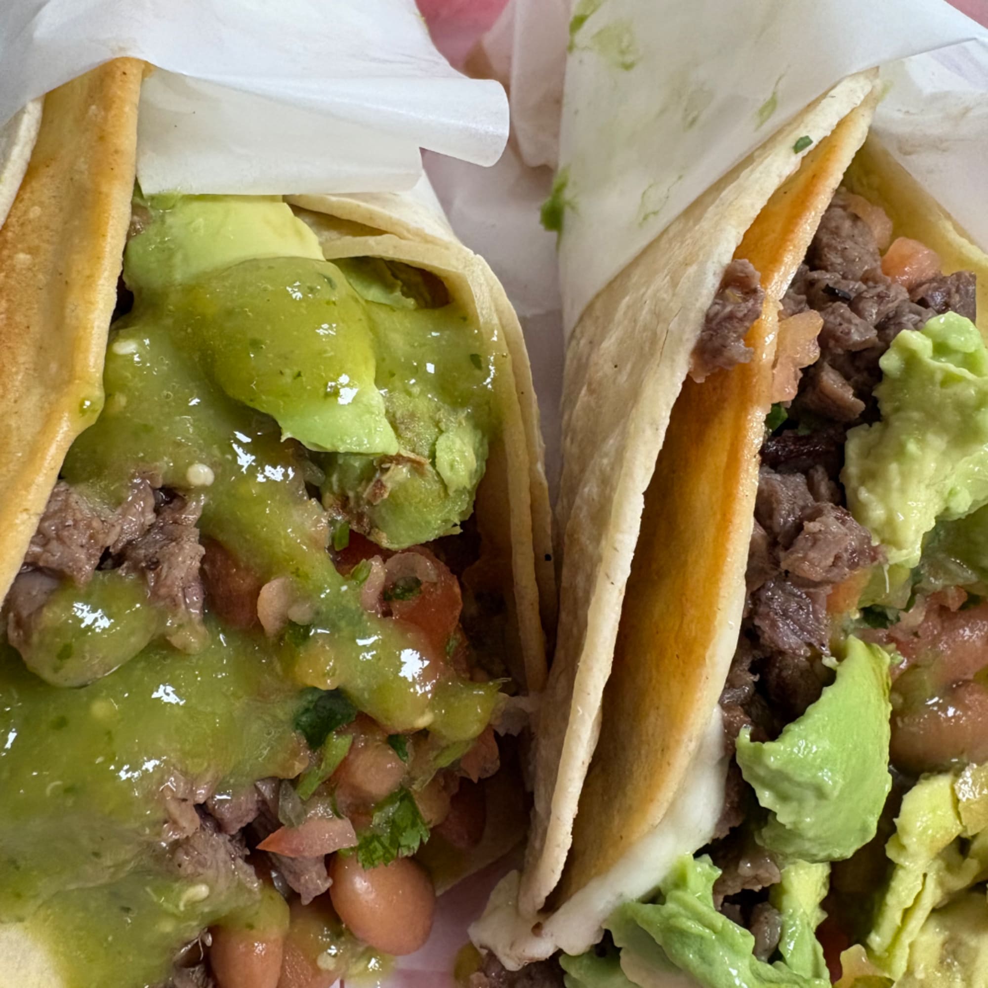 Two beef tacos topped with green salsa and avocado