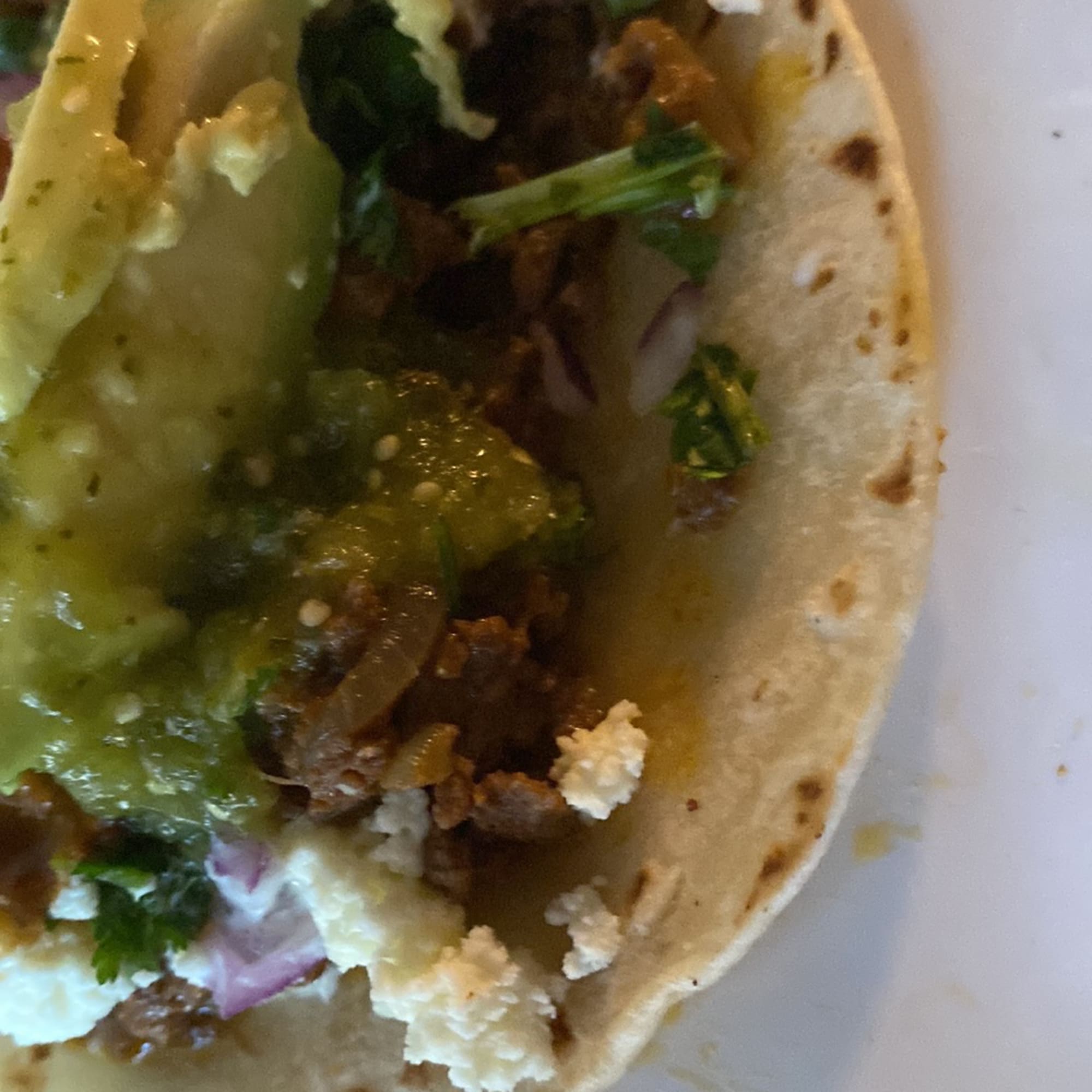 Close-up of a taco with green salsa and crumbled cheese on a plate