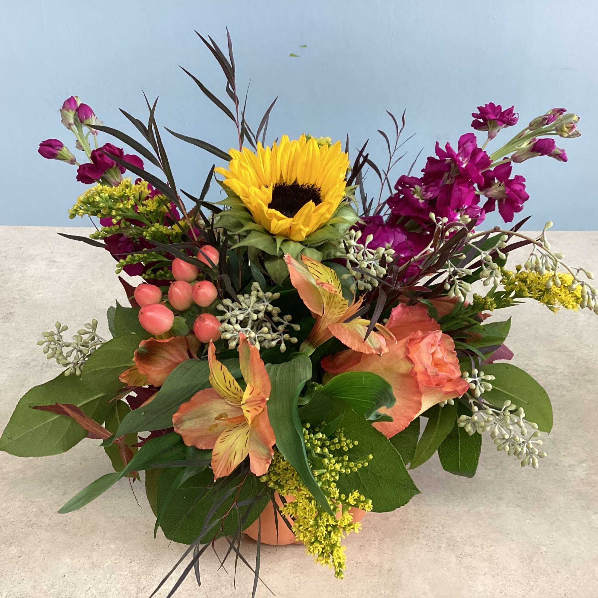 Mixed bouquet with a sunflower, pink blooms, and peach flowers in a low container